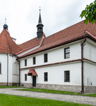 Zdjęcie nr 19: Kościół murowany z cegły i kamienia, tynkowany, orientowany, jednonawowy z kaplicami. Prezbiterium wydłużone, zamknięte trójbocznie, odchylone na południe od osi nawy, przy północnej ścianie niewielka, prostokątna dawna zakrystia (obecnie kruchta), przy południowej dobudowana wtórnie piętrowa dwuczęściowa zakrystia ze skarbcem, od wschodu, na zewnętrznej ścianie kościoła Ogrojec. Nawa główna szersza od prezbiterium, na rzucie prostokąta, od południa wieloboczna kaplica Najświętszego Serca Pana Jezusa (dawniej Przemienienia Pańskiego), od północy i południa dobudowane kaplice boczne na planie prostokąta, północna dwukrotnie większa od południowej, od zachodu wieża na planie kwadratu. Prezbiterium i nawa nakryte sklepieniami pozornymi, oddzielone od ścian gzymsem przebiegającym przez całe wnętrze, łuk tęczowy półkolisty, wewnątrz ujęty pilastrami. Dawne, ostrołukowe okna znajdują się w ścianach nawy głównej. Dostęp do kaplicy i naw bocznych z nawy głównej przez wysokie przejścia arkadowe, w północnej części nawy ujęte opaskami tynkowymi, w północno-zachodniej przejście z barokowym, kamiennym portalem (dawne wejście do kościoła). W starej zakrystii dwa gotyckie, kamienne, ostrołukowe portale oraz gotyckie okno. W wielobocznej kaplicy sklepienie kolebkowe z lunetami, w kaplicach bocznych oraz w nowej zakrystii stropy żelbetowe i sufity tynkowe. Elewacje tynkowane, z obłożoną kamieniem partią cokołu, ściana północna dawnej zakrystii z odsłoniętym wątkiem kamiennym oraz narożną przyporą, wieloboczna kaplica oszkarpowana w narożach. Do wschodniej ściany prezbiterium dobudowany kamienny Ogrójec z arkadą, zwieńczony gzymsem oraz schodkowym szczytem z kamiennymi figurami. Wejścia do kościoła przez kaplice boczne od północy i zachodu oraz przez kruchtę w przyziemiu wieży. Okna w formie stojącego prostokąta w ścianach kaplic bocznych, nowej zakrystii, prezbiterium, okna ostrołukowe w wielobocznej kaplicy. Wieża smukła, trójkondygnacyjna, bez podziałów architektonicznych z oknami na poziomie każdej kondygnacji, zwieńczona hełmem baniastym. Nawa główna i prezbiterium nakryte dachem dwuspadowym, niższe nawy boczne również. W miejscu połączenia nawy i prezbiterium wieżyczka na sygnaturkę. Kaplica przekryta dachem ostrosłupowym, nowa zakrystia i skarbiec dachem trójspadowym, stara zakrystia pulpitowym. 
