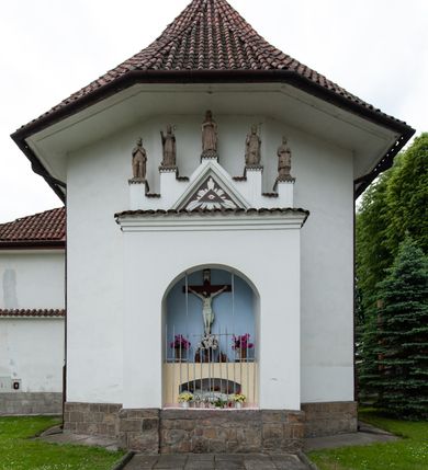 Zdjęcie nr 3: Kościół murowany z cegły i kamienia, tynkowany, orientowany, jednonawowy z kaplicami. Prezbiterium wydłużone, zamknięte trójbocznie, odchylone na południe od osi nawy, przy północnej ścianie niewielka, prostokątna dawna zakrystia (obecnie kruchta), przy południowej dobudowana wtórnie piętrowa dwuczęściowa zakrystia ze skarbcem, od wschodu, na zewnętrznej ścianie kościoła Ogrojec. Nawa główna szersza od prezbiterium, na rzucie prostokąta, od południa wieloboczna kaplica Najświętszego Serca Pana Jezusa (dawniej Przemienienia Pańskiego), od północy i południa dobudowane kaplice boczne na planie prostokąta, północna dwukrotnie większa od południowej, od zachodu wieża na planie kwadratu. Prezbiterium i nawa nakryte sklepieniami pozornymi, oddzielone od ścian gzymsem przebiegającym przez całe wnętrze, łuk tęczowy półkolisty, wewnątrz ujęty pilastrami. Dawne, ostrołukowe okna znajdują się w ścianach nawy głównej. Dostęp do kaplicy i naw bocznych z nawy głównej przez wysokie przejścia arkadowe, w północnej części nawy ujęte opaskami tynkowymi, w północno-zachodniej przejście z barokowym, kamiennym portalem (dawne wejście do kościoła). W starej zakrystii dwa gotyckie, kamienne, ostrołukowe portale oraz gotyckie okno. W wielobocznej kaplicy sklepienie kolebkowe z lunetami, w kaplicach bocznych oraz w nowej zakrystii stropy żelbetowe i sufity tynkowe. Elewacje tynkowane, z obłożoną kamieniem partią cokołu, ściana północna dawnej zakrystii z odsłoniętym wątkiem kamiennym oraz narożną przyporą, wieloboczna kaplica oszkarpowana w narożach. Do wschodniej ściany prezbiterium dobudowany kamienny Ogrójec z arkadą, zwieńczony gzymsem oraz schodkowym szczytem z kamiennymi figurami. Wejścia do kościoła przez kaplice boczne od północy i zachodu oraz przez kruchtę w przyziemiu wieży. Okna w formie stojącego prostokąta w ścianach kaplic bocznych, nowej zakrystii, prezbiterium, okna ostrołukowe w wielobocznej kaplicy. Wieża smukła, trójkondygnacyjna, bez podziałów architektonicznych z oknami na poziomie każdej kondygnacji, zwieńczona hełmem baniastym. Nawa główna i prezbiterium nakryte dachem dwuspadowym, niższe nawy boczne również. W miejscu połączenia nawy i prezbiterium wieżyczka na sygnaturkę. Kaplica przekryta dachem ostrosłupowym, nowa zakrystia i skarbiec dachem trójspadowym, stara zakrystia pulpitowym. 
