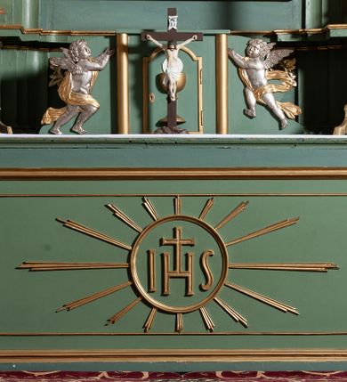 Zdjęcie nr 17: Nastawa architektoniczna, jednoosiowa, dwukondygnacyjna, ustawiona na niewielkim cokole. Ołtarz drewniany, prostopadłościenny, z drewnianą mensą, ustawiony na dwustopniowej podstawie. Antepedium ujęte ramą, w jego polu płycina dekorowana w narożach ornamentem roślinnym, pośrodku medalion z monogramem IHS w glorii promienistej. Na ołtarzu ustawione jest tabernakulum w formie drewnianej skrzynki flankowanej półwalcami oraz falistymi spływami z nałożonymi płaskorzeźbionymi postaciami adorujących puttów. Drzwiczki w kształcie stojącego prostokąta zamkniętego łukiem segmentowym nadwieszonym z kielichem i hostią w polu. 
Pierwsza kondygnacja flankowana jest zwielokrotnionymi pilastrami i stojącą przed nimi parą kolumn o kapitelach kompozytowych, dźwigających pełne belkowanie, z gzymsem dekorowanym kimationem, wyłamane na ich osi, z przerwanym architrawem nad polem środkowym. Na belkowaniu, na osiach kolumn przerwany, falisty przyczółek. W polu środkowym nisza w kształcie stojącego prostokąta zamkniętego łukiem segmentowym nadwieszonym, ujęta profilowaną ramą z obrazem Najświętszego Serca Pana Jezusa w formie stojącego prostokąta w osobnej, profilowanej ramie. Druga kondygnacja ustawiona na niewielkim cokole, flankowana zdwojonymi pilastrami i stojącą przed nimi parą kolumn o kapitelach kompozytowych, dźwigających pełne belkowanie z gzymsem dekorowanym kimationem, wyłamane na ich osi oraz przerwany półkolisty przyczółek. Nad polem, w partii belkowania medalion z przedstawieniem Gorejącego Serca w glorii promienistej, flankowany główkami anielskimi. W polu obraz w kształcie stojącego prostokąta ujętego profilowaną rama z przedstawieniem św. Franciszka obejmującego Chrystusa na krzyżu (amplexus). Obie kondygnacje ujęte uszami, pierwsza utworzonymi ze stylizowanego akantu, druga ze stylizowanego ornamentu roślinnego. Cokoły i belkowanie pierwszej kondygnacji dekorowane stylizowanym ornamentem roślinnym. Struktura ołtarza polichromowana w kolorze jasnozielonym, kolumny i profile pozłocone, ornamentyka pozłocona i posrebrzona. 