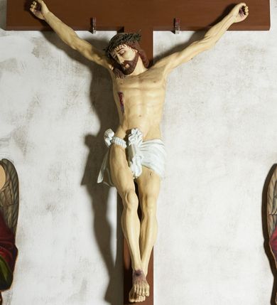 Zdjęcie nr 2: Figura umarłego Chrystusa przybita trzema gwoździami do krzyża o prostym zakończeniu ramion. Ciało w dużym zwisie, o ramionach przyjmujących kształt szerokiego „V”, na lekko ugiętych nogach, ze stopami skrzyżowanymi w układzie prawa na lewą, głowa opada na prawy bark. Twarz ma szczupłą, o dużych, zamkniętych oczach, wąskim nosie i ustach, okoloną krótką brodą i brązowymi włosami, sięgającymi ramion. Na głowie ma koronę cierniową. Ciało ma szczupłe i umięśnione, zwłaszcza w partii ramion i nóg, klatka piersiowa o delikatnie podkreślonej muskulaturze. W prawym boku rana z rzeźbionymi kroplami krwi. Białe, krótkie perizonium zawieszone na podwójnym sznurze, odsłaniające prawe udo, ze zwisem tkaniny przy prawym boku i w partii podbrzusza. Polichromia ciała naturalistyczna z zaznaczonymi śladami męki.  Na zakończeniu pionowej belki krzyża zwój z napisem „I. N. / R. I.”