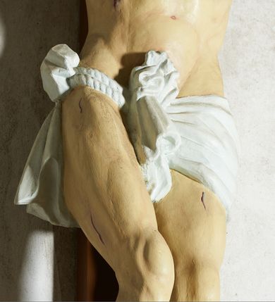 Zdjęcie nr 5: Figura umarłego Chrystusa przybita trzema gwoździami do krzyża o prostym zakończeniu ramion. Ciało w dużym zwisie, o ramionach przyjmujących kształt szerokiego „V”, na lekko ugiętych nogach, ze stopami skrzyżowanymi w układzie prawa na lewą, głowa opada na prawy bark. Twarz ma szczupłą, o dużych, zamkniętych oczach, wąskim nosie i ustach, okoloną krótką brodą i brązowymi włosami, sięgającymi ramion. Na głowie ma koronę cierniową. Ciało ma szczupłe i umięśnione, zwłaszcza w partii ramion i nóg, klatka piersiowa o delikatnie podkreślonej muskulaturze. W prawym boku rana z rzeźbionymi kroplami krwi. Białe, krótkie perizonium zawieszone na podwójnym sznurze, odsłaniające prawe udo, ze zwisem tkaniny przy prawym boku i w partii podbrzusza. Polichromia ciała naturalistyczna z zaznaczonymi śladami męki.  Na zakończeniu pionowej belki krzyża zwój z napisem „I. N. / R. I.”