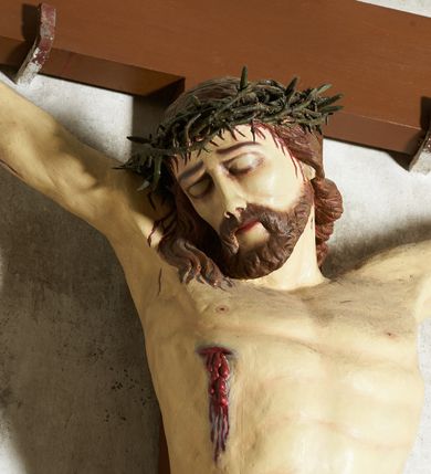 Zdjęcie nr 3: Figura umarłego Chrystusa przybita trzema gwoździami do krzyża o prostym zakończeniu ramion. Ciało w dużym zwisie, o ramionach przyjmujących kształt szerokiego „V”, na lekko ugiętych nogach, ze stopami skrzyżowanymi w układzie prawa na lewą, głowa opada na prawy bark. Twarz ma szczupłą, o dużych, zamkniętych oczach, wąskim nosie i ustach, okoloną krótką brodą i brązowymi włosami, sięgającymi ramion. Na głowie ma koronę cierniową. Ciało ma szczupłe i umięśnione, zwłaszcza w partii ramion i nóg, klatka piersiowa o delikatnie podkreślonej muskulaturze. W prawym boku rana z rzeźbionymi kroplami krwi. Białe, krótkie perizonium zawieszone na podwójnym sznurze, odsłaniające prawe udo, ze zwisem tkaniny przy prawym boku i w partii podbrzusza. Polichromia ciała naturalistyczna z zaznaczonymi śladami męki.  Na zakończeniu pionowej belki krzyża zwój z napisem „I. N. / R. I.”