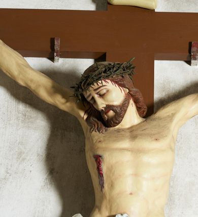 Zdjęcie nr 4: Figura umarłego Chrystusa przybita trzema gwoździami do krzyża o prostym zakończeniu ramion. Ciało w dużym zwisie, o ramionach przyjmujących kształt szerokiego „V”, na lekko ugiętych nogach, ze stopami skrzyżowanymi w układzie prawa na lewą, głowa opada na prawy bark. Twarz ma szczupłą, o dużych, zamkniętych oczach, wąskim nosie i ustach, okoloną krótką brodą i brązowymi włosami, sięgającymi ramion. Na głowie ma koronę cierniową. Ciało ma szczupłe i umięśnione, zwłaszcza w partii ramion i nóg, klatka piersiowa o delikatnie podkreślonej muskulaturze. W prawym boku rana z rzeźbionymi kroplami krwi. Białe, krótkie perizonium zawieszone na podwójnym sznurze, odsłaniające prawe udo, ze zwisem tkaniny przy prawym boku i w partii podbrzusza. Polichromia ciała naturalistyczna z zaznaczonymi śladami męki.  Na zakończeniu pionowej belki krzyża zwój z napisem „I. N. / R. I.”