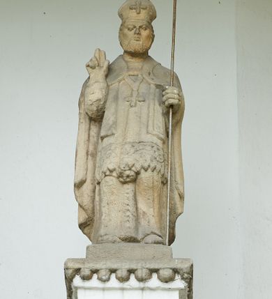 Zdjęcie nr 4: Ogrójec w formie murowanego, tynkowanego wykusza z wnęką w formie stojącego prostokąta zamkniętego łukiem odcinkowym; ustawiony na kamiennej podmurówce, zakończony profilowanym gzymsem i daszkiem okapowym. Ogrójec wieńczy szczyt w formie cokołu z wyodrębnionymi pięcioma postumentami w układzie schodkowym, na których stoją kamienne figury. Pośrodku cokołu rzeźbione w zaprawie Oko Opatrzności w trójkątnym polu, ujętym profilowaną opaską tynkową. Na postumentach od lewej figury św. Ludwika, św. Stanisława z Piotrowinem, Matki Boskiej Niepokalanie Poczętej, św. Wojciecha i św. Walentego. 
Święty Ludwik ukazany frontalnie, z rękami złożonymi w geście modlitwy. Twarz ma okoloną krótkimi włosami i brodą. Ubrany jest w krótką tunikę i spodnie, na nogach ma wysokie buty. Na ramiona ma narzucony płaszcz, opadający na plecy, zaś przez tors przewiązany pas z mieczem, znajdującym się przy lewym boku, na głowie korona zamknięta. 
Święty Stanisław ukazany frontalnie, obie ręce ma ugięte i wyciągnięte do przodu, w lewej trzyma pastorał. Twarz ma okoloną krótkimi włosami. Ubrany jest w albę, rokietę i kapę, na piersi ma krzyż pektoralny, zaś na głowie infułę. U jego nóg leżąca półpostać Piotrowina. 
Matka Boska ukazana frontalnie, stoi na półkuli z wężem, obie dłonie ma złożone na piersi. Twarz ma okoloną długimi włosami, opadającymi na ramiona. Ubrana jest w suknię przepasaną w talii oraz płaszcz zapięty na piersi i opadający kaskadowo po bokach postaci. 
Święty Wojciech ukazany frontalnie, w kontrapoście, w lewej ręce trzyma laskę zakończoną krzyżem, prawą unosi w geście błogosławieństwa. Twarz ma okoloną krótką bodą i włosami. Ubrany jest w albę, rokietę, stułę i kapę, na piersi ma krzyż pektoralny, na dłoniach rękawiczki, a na głowie infułę z krzyżem. 
Święty Walenty ukazany frontalnie, w obu ugiętych rękach trzyma z przodu otwartą księgę. Twarz ma okoloną krótkimi włosami. Ubrany jest w sutannę, komżę, stułę, a na głowie ma biret. 
W dolnej części wnęki Ogrójca nisza w formie leżącego prostokąta zamkniętego łukiem odcinkowym, wewnątrz figura Chrystusa do grobu. Ponad nią zawieszony krucyfiks.
