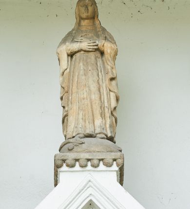 Zdjęcie nr 6: Ogrójec w formie murowanego, tynkowanego wykusza z wnęką w formie stojącego prostokąta zamkniętego łukiem odcinkowym; ustawiony na kamiennej podmurówce, zakończony profilowanym gzymsem i daszkiem okapowym. Ogrójec wieńczy szczyt w formie cokołu z wyodrębnionymi pięcioma postumentami w układzie schodkowym, na których stoją kamienne figury. Pośrodku cokołu rzeźbione w zaprawie Oko Opatrzności w trójkątnym polu, ujętym profilowaną opaską tynkową. Na postumentach od lewej figury św. Ludwika, św. Stanisława z Piotrowinem, Matki Boskiej Niepokalanie Poczętej, św. Wojciecha i św. Walentego. 
Święty Ludwik ukazany frontalnie, z rękami złożonymi w geście modlitwy. Twarz ma okoloną krótkimi włosami i brodą. Ubrany jest w krótką tunikę i spodnie, na nogach ma wysokie buty. Na ramiona ma narzucony płaszcz, opadający na plecy, zaś przez tors przewiązany pas z mieczem, znajdującym się przy lewym boku, na głowie korona zamknięta. 
Święty Stanisław ukazany frontalnie, obie ręce ma ugięte i wyciągnięte do przodu, w lewej trzyma pastorał. Twarz ma okoloną krótkimi włosami. Ubrany jest w albę, rokietę i kapę, na piersi ma krzyż pektoralny, zaś na głowie infułę. U jego nóg leżąca półpostać Piotrowina. 
Matka Boska ukazana frontalnie, stoi na półkuli z wężem, obie dłonie ma złożone na piersi. Twarz ma okoloną długimi włosami, opadającymi na ramiona. Ubrana jest w suknię przepasaną w talii oraz płaszcz zapięty na piersi i opadający kaskadowo po bokach postaci. 
Święty Wojciech ukazany frontalnie, w kontrapoście, w lewej ręce trzyma laskę zakończoną krzyżem, prawą unosi w geście błogosławieństwa. Twarz ma okoloną krótką bodą i włosami. Ubrany jest w albę, rokietę, stułę i kapę, na piersi ma krzyż pektoralny, na dłoniach rękawiczki, a na głowie infułę z krzyżem. 
Święty Walenty ukazany frontalnie, w obu ugiętych rękach trzyma z przodu otwartą księgę. Twarz ma okoloną krótkimi włosami. Ubrany jest w sutannę, komżę, stułę, a na głowie ma biret. 
W dolnej części wnęki Ogrójca nisza w formie leżącego prostokąta zamkniętego łukiem odcinkowym, wewnątrz figura Chrystusa do grobu. Ponad nią zawieszony krucyfiks.
