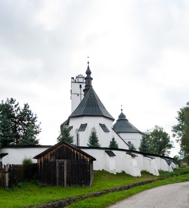 Zdjęcie nr 47: Kościół orientowany, murowany z kamienia, jednonawowy, z prostokątną, trójprzęsłową nawą oraz węższym dwuprzęsłowym prezbiterium zamkniętym trójbocznie, z niewielką prostokątną zakrystią przy północnej ścianie. Od zachodu wieża na planie kwadratu, do północnej ściany nawy dobudowana kaplica Matki Boskiej Karmelitańskiej, do południowej niewielka kruchta. Prezbiterium sklepione żebrowo z jednym rzeźbionym kroksztynem; żebra pokryte późniejszą dekoracją stiukową. Nawa wtórnie sklepiona kolebką z lunetami na gurtach, rozczłonkowana opilastrowanymi półfilarami. Pilastry i zacheuszki ozdobione stiukową ornamentacją. Do zakrystii prowadzi kamienny portal. Kościół opięty grubymi szkarpami jednouskokowymi, nakrytymi daszkami. W dwóch oknach prezbiterium i jednym nawy od południa kamienne maswerki; w zakrystii od wschodu wąskie okienko, tzw. romańskie. W pólnocno-wschodnim narożniku nawy wtórnie wkomponowany rzeźbiony, bardzo zniszczony kroksztyn. Z południowej kruchty do nawy prowadzi kamienny portal o trzech parach kolumienek dźwigających archiwolty. Nawa i prezbiterium nakryte dachem, na ich styku wieżyczka na sygnaturkę. Wieża smukła, bez podziałów architektonicznych, ściany najwyższej kondygnacji cofnięte w głąb, przy krawędzi kamienne kroksztyny, pozostałe po niezachowanej drewnianej hurdycji. Wieża zwieńczona ceglaną attyką, zasłaniającą dwuspadowy dach. W górnej części jej trzonu okna usytuowane z czterech stron. W miejscu hurdycji, na zachodniej ścianie zegar. 

Kościół otoczony niskim murem kamiennym; od zachodu dzwonnica bramna na planie kwadratu z niesklepioną sienią przejściową, nakryta blaszanym hełmem; od południa i od wschodu bramki nakryte hełmami, przy czym jeden pokryty jest gontem, drugi blachą.