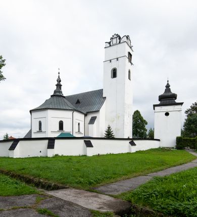 Zdjęcie nr 35: Kościół orientowany, murowany z kamienia, jednonawowy, z prostokątną, trójprzęsłową nawą oraz węższym dwuprzęsłowym prezbiterium zamkniętym trójbocznie, z niewielką prostokątną zakrystią przy północnej ścianie. Od zachodu wieża na planie kwadratu, do północnej ściany nawy dobudowana kaplica Matki Boskiej Karmelitańskiej, do południowej niewielka kruchta. Prezbiterium sklepione żebrowo z jednym rzeźbionym kroksztynem; żebra pokryte późniejszą dekoracją stiukową. Nawa wtórnie sklepiona kolebką z lunetami na gurtach, rozczłonkowana opilastrowanymi półfilarami. Pilastry i zacheuszki ozdobione stiukową ornamentacją. Do zakrystii prowadzi kamienny portal. Kościół opięty grubymi szkarpami jednouskokowymi, nakrytymi daszkami. W dwóch oknach prezbiterium i jednym nawy od południa kamienne maswerki; w zakrystii od wschodu wąskie okienko, tzw. romańskie. W pólnocno-wschodnim narożniku nawy wtórnie wkomponowany rzeźbiony, bardzo zniszczony kroksztyn. Z południowej kruchty do nawy prowadzi kamienny portal o trzech parach kolumienek dźwigających archiwolty. Nawa i prezbiterium nakryte dachem, na ich styku wieżyczka na sygnaturkę. Wieża smukła, bez podziałów architektonicznych, ściany najwyższej kondygnacji cofnięte w głąb, przy krawędzi kamienne kroksztyny, pozostałe po niezachowanej drewnianej hurdycji. Wieża zwieńczona ceglaną attyką, zasłaniającą dwuspadowy dach. W górnej części jej trzonu okna usytuowane z czterech stron. W miejscu hurdycji, na zachodniej ścianie zegar. 

Kościół otoczony niskim murem kamiennym; od zachodu dzwonnica bramna na planie kwadratu z niesklepioną sienią przejściową, nakryta blaszanym hełmem; od południa i od wschodu bramki nakryte hełmami, przy czym jeden pokryty jest gontem, drugi blachą.
