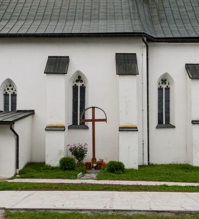 Zdjęcie nr 5: Kościół orientowany, murowany z kamienia, jednonawowy, z prostokątną, trójprzęsłową nawą oraz węższym dwuprzęsłowym prezbiterium zamkniętym trójbocznie, z niewielką prostokątną zakrystią przy północnej ścianie. Od zachodu wieża na planie kwadratu, do północnej ściany nawy dobudowana kaplica Matki Boskiej Karmelitańskiej, do południowej niewielka kruchta. Prezbiterium sklepione żebrowo z jednym rzeźbionym kroksztynem; żebra pokryte późniejszą dekoracją stiukową. Nawa wtórnie sklepiona kolebką z lunetami na gurtach, rozczłonkowana opilastrowanymi półfilarami. Pilastry i zacheuszki ozdobione stiukową ornamentacją. Do zakrystii prowadzi kamienny portal. Kościół opięty grubymi szkarpami jednouskokowymi, nakrytymi daszkami. W dwóch oknach prezbiterium i jednym nawy od południa kamienne maswerki; w zakrystii od wschodu wąskie okienko, tzw. romańskie. W pólnocno-wschodnim narożniku nawy wtórnie wkomponowany rzeźbiony, bardzo zniszczony kroksztyn. Z południowej kruchty do nawy prowadzi kamienny portal o trzech parach kolumienek dźwigających archiwolty. Nawa i prezbiterium nakryte dachem, na ich styku wieżyczka na sygnaturkę. Wieża smukła, bez podziałów architektonicznych, ściany najwyższej kondygnacji cofnięte w głąb, przy krawędzi kamienne kroksztyny, pozostałe po niezachowanej drewnianej hurdycji. Wieża zwieńczona ceglaną attyką, zasłaniającą dwuspadowy dach. W górnej części jej trzonu okna usytuowane z czterech stron. W miejscu hurdycji, na zachodniej ścianie zegar. 

Kościół otoczony niskim murem kamiennym; od zachodu dzwonnica bramna na planie kwadratu z niesklepioną sienią przejściową, nakryta blaszanym hełmem; od południa i od wschodu bramki nakryte hełmami, przy czym jeden pokryty jest gontem, drugi blachą.