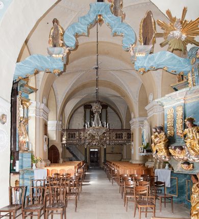 Zdjęcie nr 20: Kościół orientowany, murowany z kamienia, jednonawowy, z prostokątną, trójprzęsłową nawą oraz węższym dwuprzęsłowym prezbiterium zamkniętym trójbocznie, z niewielką prostokątną zakrystią przy północnej ścianie. Od zachodu wieża na planie kwadratu, do północnej ściany nawy dobudowana kaplica Matki Boskiej Karmelitańskiej, do południowej niewielka kruchta. Prezbiterium sklepione żebrowo z jednym rzeźbionym kroksztynem; żebra pokryte późniejszą dekoracją stiukową. Nawa wtórnie sklepiona kolebką z lunetami na gurtach, rozczłonkowana opilastrowanymi półfilarami. Pilastry i zacheuszki ozdobione stiukową ornamentacją. Do zakrystii prowadzi kamienny portal. Kościół opięty grubymi szkarpami jednouskokowymi, nakrytymi daszkami. W dwóch oknach prezbiterium i jednym nawy od południa kamienne maswerki; w zakrystii od wschodu wąskie okienko, tzw. romańskie. W pólnocno-wschodnim narożniku nawy wtórnie wkomponowany rzeźbiony, bardzo zniszczony kroksztyn. Z południowej kruchty do nawy prowadzi kamienny portal o trzech parach kolumienek dźwigających archiwolty. Nawa i prezbiterium nakryte dachem, na ich styku wieżyczka na sygnaturkę. Wieża smukła, bez podziałów architektonicznych, ściany najwyższej kondygnacji cofnięte w głąb, przy krawędzi kamienne kroksztyny, pozostałe po niezachowanej drewnianej hurdycji. Wieża zwieńczona ceglaną attyką, zasłaniającą dwuspadowy dach. W górnej części jej trzonu okna usytuowane z czterech stron. W miejscu hurdycji, na zachodniej ścianie zegar. 

Kościół otoczony niskim murem kamiennym; od zachodu dzwonnica bramna na planie kwadratu z niesklepioną sienią przejściową, nakryta blaszanym hełmem; od południa i od wschodu bramki nakryte hełmami, przy czym jeden pokryty jest gontem, drugi blachą.