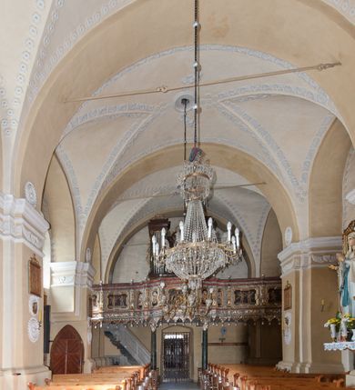 Zdjęcie nr 31: Kościół orientowany, murowany z kamienia, jednonawowy, z prostokątną, trójprzęsłową nawą oraz węższym dwuprzęsłowym prezbiterium zamkniętym trójbocznie, z niewielką prostokątną zakrystią przy północnej ścianie. Od zachodu wieża na planie kwadratu, do północnej ściany nawy dobudowana kaplica Matki Boskiej Karmelitańskiej, do południowej niewielka kruchta. Prezbiterium sklepione żebrowo z jednym rzeźbionym kroksztynem; żebra pokryte późniejszą dekoracją stiukową. Nawa wtórnie sklepiona kolebką z lunetami na gurtach, rozczłonkowana opilastrowanymi półfilarami. Pilastry i zacheuszki ozdobione stiukową ornamentacją. Do zakrystii prowadzi kamienny portal. Kościół opięty grubymi szkarpami jednouskokowymi, nakrytymi daszkami. W dwóch oknach prezbiterium i jednym nawy od południa kamienne maswerki; w zakrystii od wschodu wąskie okienko, tzw. romańskie. W pólnocno-wschodnim narożniku nawy wtórnie wkomponowany rzeźbiony, bardzo zniszczony kroksztyn. Z południowej kruchty do nawy prowadzi kamienny portal o trzech parach kolumienek dźwigających archiwolty. Nawa i prezbiterium nakryte dachem, na ich styku wieżyczka na sygnaturkę. Wieża smukła, bez podziałów architektonicznych, ściany najwyższej kondygnacji cofnięte w głąb, przy krawędzi kamienne kroksztyny, pozostałe po niezachowanej drewnianej hurdycji. Wieża zwieńczona ceglaną attyką, zasłaniającą dwuspadowy dach. W górnej części jej trzonu okna usytuowane z czterech stron. W miejscu hurdycji, na zachodniej ścianie zegar. 

Kościół otoczony niskim murem kamiennym; od zachodu dzwonnica bramna na planie kwadratu z niesklepioną sienią przejściową, nakryta blaszanym hełmem; od południa i od wschodu bramki nakryte hełmami, przy czym jeden pokryty jest gontem, drugi blachą.