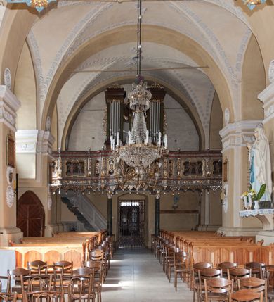 Zdjęcie nr 30: Kościół orientowany, murowany z kamienia, jednonawowy, z prostokątną, trójprzęsłową nawą oraz węższym dwuprzęsłowym prezbiterium zamkniętym trójbocznie, z niewielką prostokątną zakrystią przy północnej ścianie. Od zachodu wieża na planie kwadratu, do północnej ściany nawy dobudowana kaplica Matki Boskiej Karmelitańskiej, do południowej niewielka kruchta. Prezbiterium sklepione żebrowo z jednym rzeźbionym kroksztynem; żebra pokryte późniejszą dekoracją stiukową. Nawa wtórnie sklepiona kolebką z lunetami na gurtach, rozczłonkowana opilastrowanymi półfilarami. Pilastry i zacheuszki ozdobione stiukową ornamentacją. Do zakrystii prowadzi kamienny portal. Kościół opięty grubymi szkarpami jednouskokowymi, nakrytymi daszkami. W dwóch oknach prezbiterium i jednym nawy od południa kamienne maswerki; w zakrystii od wschodu wąskie okienko, tzw. romańskie. W pólnocno-wschodnim narożniku nawy wtórnie wkomponowany rzeźbiony, bardzo zniszczony kroksztyn. Z południowej kruchty do nawy prowadzi kamienny portal o trzech parach kolumienek dźwigających archiwolty. Nawa i prezbiterium nakryte dachem, na ich styku wieżyczka na sygnaturkę. Wieża smukła, bez podziałów architektonicznych, ściany najwyższej kondygnacji cofnięte w głąb, przy krawędzi kamienne kroksztyny, pozostałe po niezachowanej drewnianej hurdycji. Wieża zwieńczona ceglaną attyką, zasłaniającą dwuspadowy dach. W górnej części jej trzonu okna usytuowane z czterech stron. W miejscu hurdycji, na zachodniej ścianie zegar. 

Kościół otoczony niskim murem kamiennym; od zachodu dzwonnica bramna na planie kwadratu z niesklepioną sienią przejściową, nakryta blaszanym hełmem; od południa i od wschodu bramki nakryte hełmami, przy czym jeden pokryty jest gontem, drugi blachą.