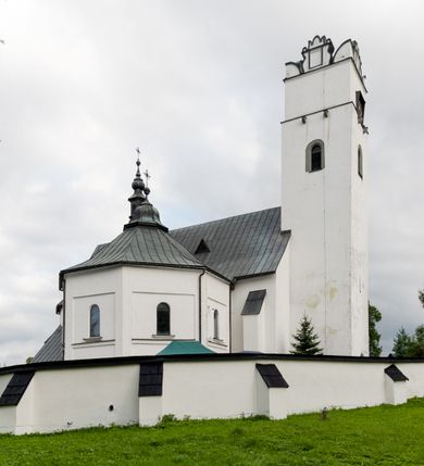 Zdjęcie nr 1: Kościół orientowany, murowany z kamienia, jednonawowy, z prostokątną, trójprzęsłową nawą oraz węższym dwuprzęsłowym prezbiterium zamkniętym trójbocznie, z niewielką prostokątną zakrystią przy północnej ścianie. Od zachodu wieża na planie kwadratu, do północnej ściany nawy dobudowana kaplica Matki Boskiej Karmelitańskiej, do południowej niewielka kruchta. Prezbiterium sklepione żebrowo z jednym rzeźbionym kroksztynem; żebra pokryte późniejszą dekoracją stiukową. Nawa wtórnie sklepiona kolebką z lunetami na gurtach, rozczłonkowana opilastrowanymi półfilarami. Pilastry i zacheuszki ozdobione stiukową ornamentacją. Do zakrystii prowadzi kamienny portal. Kościół opięty grubymi szkarpami jednouskokowymi, nakrytymi daszkami. W dwóch oknach prezbiterium i jednym nawy od południa kamienne maswerki; w zakrystii od wschodu wąskie okienko, tzw. romańskie. W pólnocno-wschodnim narożniku nawy wtórnie wkomponowany rzeźbiony, bardzo zniszczony kroksztyn. Z południowej kruchty do nawy prowadzi kamienny portal o trzech parach kolumienek dźwigających archiwolty. Nawa i prezbiterium nakryte dachem, na ich styku wieżyczka na sygnaturkę. Wieża smukła, bez podziałów architektonicznych, ściany najwyższej kondygnacji cofnięte w głąb, przy krawędzi kamienne kroksztyny, pozostałe po niezachowanej drewnianej hurdycji. Wieża zwieńczona ceglaną attyką, zasłaniającą dwuspadowy dach. W górnej części jej trzonu okna usytuowane z czterech stron. W miejscu hurdycji, na zachodniej ścianie zegar. 

Kościół otoczony niskim murem kamiennym; od zachodu dzwonnica bramna na planie kwadratu z niesklepioną sienią przejściową, nakryta blaszanym hełmem; od południa i od wschodu bramki nakryte hełmami, przy czym jeden pokryty jest gontem, drugi blachą.