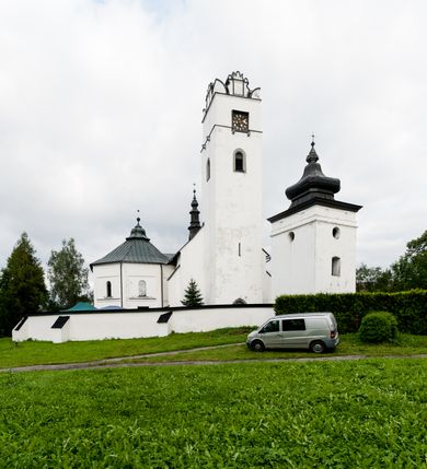 Zdjęcie nr 45: Kościół orientowany, murowany z kamienia, jednonawowy, z prostokątną, trójprzęsłową nawą oraz węższym dwuprzęsłowym prezbiterium zamkniętym trójbocznie, z niewielką prostokątną zakrystią przy północnej ścianie. Od zachodu wieża na planie kwadratu, do północnej ściany nawy dobudowana kaplica Matki Boskiej Karmelitańskiej, do południowej niewielka kruchta. Prezbiterium sklepione żebrowo z jednym rzeźbionym kroksztynem; żebra pokryte późniejszą dekoracją stiukową. Nawa wtórnie sklepiona kolebką z lunetami na gurtach, rozczłonkowana opilastrowanymi półfilarami. Pilastry i zacheuszki ozdobione stiukową ornamentacją. Do zakrystii prowadzi kamienny portal. Kościół opięty grubymi szkarpami jednouskokowymi, nakrytymi daszkami. W dwóch oknach prezbiterium i jednym nawy od południa kamienne maswerki; w zakrystii od wschodu wąskie okienko, tzw. romańskie. W pólnocno-wschodnim narożniku nawy wtórnie wkomponowany rzeźbiony, bardzo zniszczony kroksztyn. Z południowej kruchty do nawy prowadzi kamienny portal o trzech parach kolumienek dźwigających archiwolty. Nawa i prezbiterium nakryte dachem, na ich styku wieżyczka na sygnaturkę. Wieża smukła, bez podziałów architektonicznych, ściany najwyższej kondygnacji cofnięte w głąb, przy krawędzi kamienne kroksztyny, pozostałe po niezachowanej drewnianej hurdycji. Wieża zwieńczona ceglaną attyką, zasłaniającą dwuspadowy dach. W górnej części jej trzonu okna usytuowane z czterech stron. W miejscu hurdycji, na zachodniej ścianie zegar. 

Kościół otoczony niskim murem kamiennym; od zachodu dzwonnica bramna na planie kwadratu z niesklepioną sienią przejściową, nakryta blaszanym hełmem; od południa i od wschodu bramki nakryte hełmami, przy czym jeden pokryty jest gontem, drugi blachą.