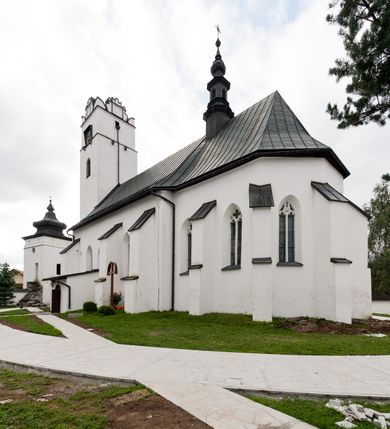 Zdjęcie nr 49: Kościół orientowany, murowany z kamienia, jednonawowy, z prostokątną, trójprzęsłową nawą oraz węższym dwuprzęsłowym prezbiterium zamkniętym trójbocznie, z niewielką prostokątną zakrystią przy północnej ścianie. Od zachodu wieża na planie kwadratu, do północnej ściany nawy dobudowana kaplica Matki Boskiej Karmelitańskiej, do południowej niewielka kruchta. Prezbiterium sklepione żebrowo z jednym rzeźbionym kroksztynem; żebra pokryte późniejszą dekoracją stiukową. Nawa wtórnie sklepiona kolebką z lunetami na gurtach, rozczłonkowana opilastrowanymi półfilarami. Pilastry i zacheuszki ozdobione stiukową ornamentacją. Do zakrystii prowadzi kamienny portal. Kościół opięty grubymi szkarpami jednouskokowymi, nakrytymi daszkami. W dwóch oknach prezbiterium i jednym nawy od południa kamienne maswerki; w zakrystii od wschodu wąskie okienko, tzw. romańskie. W pólnocno-wschodnim narożniku nawy wtórnie wkomponowany rzeźbiony, bardzo zniszczony kroksztyn. Z południowej kruchty do nawy prowadzi kamienny portal o trzech parach kolumienek dźwigających archiwolty. Nawa i prezbiterium nakryte dachem, na ich styku wieżyczka na sygnaturkę. Wieża smukła, bez podziałów architektonicznych, ściany najwyższej kondygnacji cofnięte w głąb, przy krawędzi kamienne kroksztyny, pozostałe po niezachowanej drewnianej hurdycji. Wieża zwieńczona ceglaną attyką, zasłaniającą dwuspadowy dach. W górnej części jej trzonu okna usytuowane z czterech stron. W miejscu hurdycji, na zachodniej ścianie zegar. 

Kościół otoczony niskim murem kamiennym; od zachodu dzwonnica bramna na planie kwadratu z niesklepioną sienią przejściową, nakryta blaszanym hełmem; od południa i od wschodu bramki nakryte hełmami, przy czym jeden pokryty jest gontem, drugi blachą.