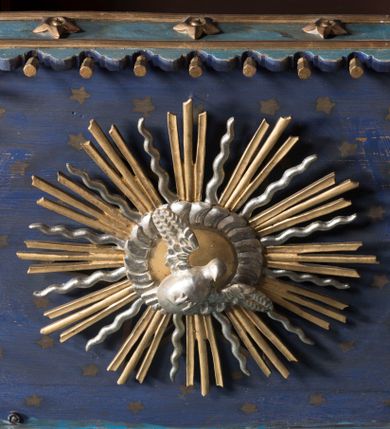 Zdjęcie nr 2: Ambona wisząca, przyścienna, z wejściem od strony zakrystii. Kosz jest na planie czworoboku o ściętych narożach, ścianki są o wklęsło-wypukłej powierzchni. Podwieszenie jest w formie profilowanego, zwężającego się ku dołowi gzymsu. W zaplecku ambony znajduje się prostokątny otwór wejściowy ujęty parą pilastrów o kanelowanych trzonach. Płytki baldachim, na rzucie czworoboku o ściętych narożach, nakryty jest spłaszczonym hełmem. Kosz ambony zdobią pojedyncze rozetki, krawędzie ujmują wąskie, żłobkowane listwy. Wzdłuż krawędzi baldachimu znajdują się pojedyncze rozetki oraz motyw lambrekinu. Podniebie zdobi płaskorzeźbiona gołębica Ducha Świętego ujęta srebrzonym wieńcem obłoków i kolistą, promienistą glorią. Struktura ambony jest marmoryzowana w odcieniach błękitu i szarości, ornamentyka jest złocona i srebrzona.
