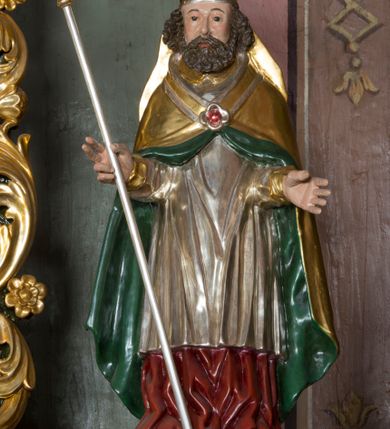 Zdjęcie nr 6: Ołtarz przyścienny, architektoniczny, jednokondygnacyjny ze zwieńczeniem i bramkami. 
Ołtarz prostopadłościenny z mensą wspartą na dwóch tralkach. Antepedium ujęte parą tralek.
Retabulum z uszakami flankowane parą kolumn korynckich o skręcanych trzonach, ustawionych na niskich wysuniętych cokołach. Podpory wspierają odcinki wyłamanego belkowania z architrawem wygiętym w łuk półkolisty. Powyżej belkowania ustawione odcinki wklęsłego przyczółka. 
Zwieńczenie prostopadłościenne z uszakami, zamknięte łukiem nadwieszanym wspieranym przez parę podwójnych pilastrów.
Po bokach ołtarza bramki o wklęsło-wypukłym wykroju z otworami drzwiowymi w kształcie stojącego prostokąta z ćwierćkoliście wklęsłymi górnymi narożami. 
Pole środkowe retabulum w formie wnęki w kształcie prostokąta zamkniętej łukiem nadwieszanym, ujętej podwójnym obramieniem o analogicznym wykroju. We wnęce obraz z przedstawieniem Matki Boskiej z Dzieciątkiem. W antepedium obraz w kształcie leżącego prostokąta z przedstawieniem kielicha z hostią adorowanego przez św. Wojciecha i nieznanego świętego. W zwieńczeniu obraz w kształcie stojącego prostokąta z przedstawieniem Trójcy Świętej ujęty profilowaną ramą.
Nad bramkami, ustawione na cokołach figury św. Wojciecha po prawej oraz św. Stanisława po lewej stronie. Na odcinkach przyczółka ukazane całopostaciowe figury uskrzydlonych aniołków. 
Uszaki ołtarza ażurowe, formowane ze skręconych liści akantu z kwiatami. Wnęka pola środkowego retabulum ujęta szeroką, ażurową ramą formowaną z liści akantu i kwiatów. Poniżej aplikowany monogram maryjny. Po bokach wnęki ornament cekinowy. Poniżej gzymsu ażurowy ornament akantowy. Trzony kolumn oplecione płaskorzeźbioną wicią winorośli. Ścianki cokołów dekorowane płycinami z rzeźbionym liściem akantu. W zwieńczeniu aplikowany rzeźbiony monogram maryjny ujęty wieńcem z koroną. 
Całość struktury ołtarza malowana na jasnobłękitny odcień z marmoryzacją w odcieniach szarości. Profilowania, ornamenty i detal architektoniczny pozłacane.
