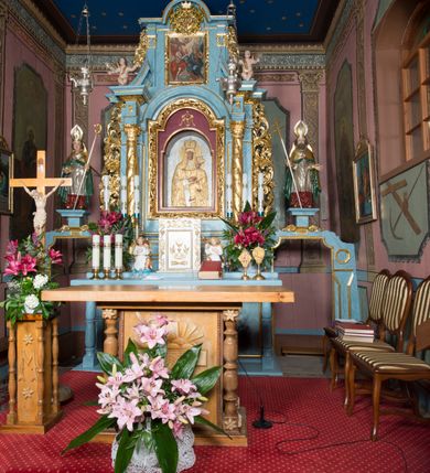 Zdjęcie nr 12: Ołtarz przyścienny, architektoniczny, jednokondygnacyjny ze zwieńczeniem i bramkami. 
Ołtarz prostopadłościenny z mensą wspartą na dwóch tralkach. Antepedium ujęte parą tralek.
Retabulum z uszakami flankowane parą kolumn korynckich o skręcanych trzonach, ustawionych na niskich wysuniętych cokołach. Podpory wspierają odcinki wyłamanego belkowania z architrawem wygiętym w łuk półkolisty. Powyżej belkowania ustawione odcinki wklęsłego przyczółka. 
Zwieńczenie prostopadłościenne z uszakami, zamknięte łukiem nadwieszanym wspieranym przez parę podwójnych pilastrów.
Po bokach ołtarza bramki o wklęsło-wypukłym wykroju z otworami drzwiowymi w kształcie stojącego prostokąta z ćwierćkoliście wklęsłymi górnymi narożami. 
Pole środkowe retabulum w formie wnęki w kształcie prostokąta zamkniętej łukiem nadwieszanym, ujętej podwójnym obramieniem o analogicznym wykroju. We wnęce obraz z przedstawieniem Matki Boskiej z Dzieciątkiem. W antepedium obraz w kształcie leżącego prostokąta z przedstawieniem kielicha z hostią adorowanego przez św. Wojciecha i nieznanego świętego. W zwieńczeniu obraz w kształcie stojącego prostokąta z przedstawieniem Trójcy Świętej ujęty profilowaną ramą.
Nad bramkami, ustawione na cokołach figury św. Wojciecha po prawej oraz św. Stanisława po lewej stronie. Na odcinkach przyczółka ukazane całopostaciowe figury uskrzydlonych aniołków. 
Uszaki ołtarza ażurowe, formowane ze skręconych liści akantu z kwiatami. Wnęka pola środkowego retabulum ujęta szeroką, ażurową ramą formowaną z liści akantu i kwiatów. Poniżej aplikowany monogram maryjny. Po bokach wnęki ornament cekinowy. Poniżej gzymsu ażurowy ornament akantowy. Trzony kolumn oplecione płaskorzeźbioną wicią winorośli. Ścianki cokołów dekorowane płycinami z rzeźbionym liściem akantu. W zwieńczeniu aplikowany rzeźbiony monogram maryjny ujęty wieńcem z koroną. 
Całość struktury ołtarza malowana na jasnobłękitny odcień z marmoryzacją w odcieniach szarości. Profilowania, ornamenty i detal architektoniczny pozłacane.
