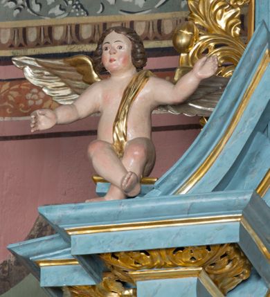 Zdjęcie nr 5: Pełnoplastyczne figury uskrzydlonych aniołków ustawionych przeciwstawnie. Postaci zostały ukazane w pozycji siedzącej, z uniesionymi wysoko rękoma i skrzyżowanymi nogami. Biodra osłonięte wąską, złota szarfą przerzuconą przez ramię. Twarze owalne, pełne, okolone puklami brązowych włosów. Karnacje ciała w naturalnym, jasnokremowym odcieniu, policzki zaróżowione.