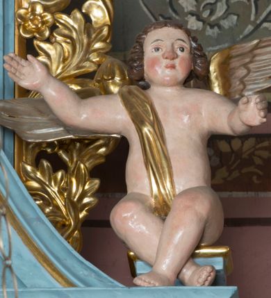 Zdjęcie nr 1: Pełnoplastyczne figury uskrzydlonych aniołków ustawionych przeciwstawnie. Postaci zostały ukazane w pozycji siedzącej, z uniesionymi wysoko rękoma i skrzyżowanymi nogami. Biodra osłonięte wąską, złota szarfą przerzuconą przez ramię. Twarze owalne, pełne, okolone puklami brązowych włosów. Karnacje ciała w naturalnym, jasnokremowym odcieniu, policzki zaróżowione.