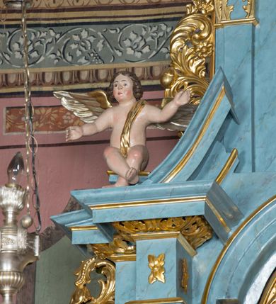 Zdjęcie nr 2: Pełnoplastyczne figury uskrzydlonych aniołków ustawionych przeciwstawnie. Postaci zostały ukazane w pozycji siedzącej, z uniesionymi wysoko rękoma i skrzyżowanymi nogami. Biodra osłonięte wąską, złota szarfą przerzuconą przez ramię. Twarze owalne, pełne, okolone puklami brązowych włosów. Karnacje ciała w naturalnym, jasnokremowym odcieniu, policzki zaróżowione.