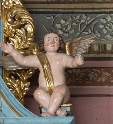 Zdjęcie nr 8: Pełnoplastyczne figury uskrzydlonych aniołków ustawionych przeciwstawnie. Postaci zostały ukazane w pozycji siedzącej, z uniesionymi wysoko rękoma i skrzyżowanymi nogami. Biodra osłonięte wąską, złota szarfą przerzuconą przez ramię. Twarze owalne, pełne, okolone puklami brązowych włosów. Karnacje ciała w naturalnym, jasnokremowym odcieniu, policzki zaróżowione.