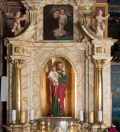 Zdjęcie nr 4: Ołtarz architektoniczny, jednokondygnacyjny, jednoosiowy ze zwieńczeniem. Ołtarz jest prostopadłościenny, z drewnianą mensą. Retabulum osadzone jest na niewysokim, zryzalitowanym cokole. Część środkową nastawy ujmuje para kolumn o korynckich kapitelach, ustawionych na tle zdwojonych pilastrów. Podpory wspierają wyłamujące się ponad nimi belkowanie przerwane w partii architrawu i fryzu. Część środkowa zaaranżowana jest w formie trójbocznej niszy o wykroju zamkniętym łukiem półkolistym, ujętej prostokątną płyciną. Zamknięte trójkątnie zwieńczenie ujęte jest parą pilastrów wspierających gzyms wieńczący. Dodatkowo po bokach znajduje się para niewysokich cokolików oraz przerwany, wklęsły przyczółek. Środkowa płycina antepedium zdobiona jest polichromowanym monogramem maryjnym, ujętym wieńcem kwiatów, płyciny po bokach zdobią wazony z kwiatami. W partii fryzu retabulum oraz na kapitelach pilastrów w zwieńczeniu są motywy rozet. Szczyt zwieńczenia jest w formie ażurowego ornamentu stylizowanej wici roślinnej, po bokach para płomienistych wazonów. W niszy części środkowej retabulum jest figura św. Józefa, w zwieńczeniu obraz w kształcie stojącego prostokąta o ściętych górnych narożach z wizerunkiem św. Antoniego Padewskiego. Na cokolikach ujmujących zwieńczenie usytuowana jest para figur siedzących aniołków.

Struktura ołtarza jest marmoryzowana w odcieniach kremu, beżów i zieleni, detal architektoniczny oraz ornamentyka są złocone.      

