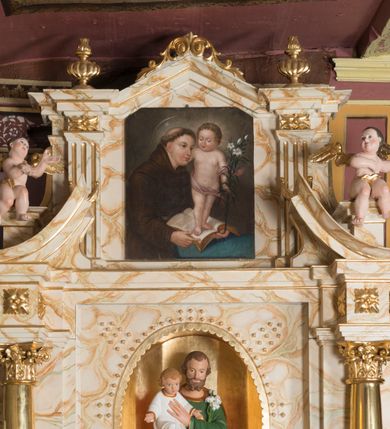 Zdjęcie nr 6: Ołtarz architektoniczny, jednokondygnacyjny, jednoosiowy ze zwieńczeniem. Ołtarz jest prostopadłościenny, z drewnianą mensą. Retabulum osadzone jest na niewysokim, zryzalitowanym cokole. Część środkową nastawy ujmuje para kolumn o korynckich kapitelach, ustawionych na tle zdwojonych pilastrów. Podpory wspierają wyłamujące się ponad nimi belkowanie przerwane w partii architrawu i fryzu. Część środkowa zaaranżowana jest w formie trójbocznej niszy o wykroju zamkniętym łukiem półkolistym, ujętej prostokątną płyciną. Zamknięte trójkątnie zwieńczenie ujęte jest parą pilastrów wspierających gzyms wieńczący. Dodatkowo po bokach znajduje się para niewysokich cokolików oraz przerwany, wklęsły przyczółek. Środkowa płycina antepedium zdobiona jest polichromowanym monogramem maryjnym, ujętym wieńcem kwiatów, płyciny po bokach zdobią wazony z kwiatami. W partii fryzu retabulum oraz na kapitelach pilastrów w zwieńczeniu są motywy rozet. Szczyt zwieńczenia jest w formie ażurowego ornamentu stylizowanej wici roślinnej, po bokach para płomienistych wazonów. W niszy części środkowej retabulum jest figura św. Józefa, w zwieńczeniu obraz w kształcie stojącego prostokąta o ściętych górnych narożach z wizerunkiem św. Antoniego Padewskiego. Na cokolikach ujmujących zwieńczenie usytuowana jest para figur siedzących aniołków.

Struktura ołtarza jest marmoryzowana w odcieniach kremu, beżów i zieleni, detal architektoniczny oraz ornamentyka są złocone.      
