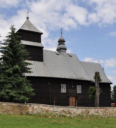 Zdjęcie nr 35: Kościół drewniany o konstrukcji zrębowej, elewacje jednolite, szalowane gontem. Wieża i kruchta zachodnia o konstrukcji słupowo-ramowej, narożne słupy nośne wzmocnione krzyżami św. Andrzeja. Więźba dachowa drewniana, krokwiowa. Budynek na kamiennym podmurowaniu. 
Kościół orientowany, jednonawowy, nawa na rzucie prostokąta zbliżonego do kwadratu, prezbiterium nieco węższe, wydłużone, zakończone trójbocznie. Do północnej ściany prezbiterium przylega zakrystia na planie prostokąta. Przy zachodniej ścianie nawy wieża na planie zbliżonym do prostokąta, o lekko ukośnej ścianie południowej. Od zachodu do wieży przylega kruchta na rzucie prostokąta. 
W przyziemiu wieży babiniec połączony z nawą wtórnym otworem w ścianie. Pomiędzy nawą a prezbiterium otwór tęczowy. Parapet chóru muzycznego w zachodniej części nawy, wsparty na czterech drewnianych kolumnach, z wejściem z nawy po drabiniastych schodach. Ściany i sklepienia pokryte polichromią z iluzjonistyczną architekturą i scenami figuralnymi. Wnętrze nakryte pułapami deskowymi w nawie i prezbiterium oraz stropem belkowym w babińcu. Otwory drzwiowe o prostokątnym wykroju zamknięte drzwiami obitymi deskami w kruchcie zachodniej, w ścianie południowej nawy oraz z prezbiterium do zakrystii. Okna w formie stojącego prostokąta. Posadzka kamienna, z płyt marmurowych. 
Elewacja frontowa jednoosiowa. Na osi wejście do kruchty zachodniej. Korpus wieży podzielony poziomo daszkami okapowymi, na froncie okno. Elewacje boczne jednolite. Korpus nawowy przepruty oknami po dwa na ścianach północnej i południowej, prezbiterium z oknem na ścianie południowej oraz dwoma okienkami na ścianach zamknięcia. Na elewacji wschodniej zawieszony krucyfiks. 
Kościół nakryty dachami dwuspadowymi, o pokryciu blaszanym, wyższym nad nawą, niższym nad prezbiterium. W połowie długości dachu, nad nawą, wbudowana wieżyczka na sygnaturkę, na ośmiobocznym, obitym blachą trzonie, z latarnią zwieńczoną niewielkim hełmem. Wieża nakryta czterospadowym daszkiem namiotowym, zwieńczona kulistą puszką i krzyżem. Kruchta nakryta osobnym daszkiem dwuspadowym, półszczytowym, zakrystia niższym dachem pulpitowym.
