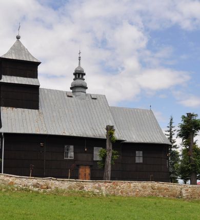 Zdjęcie nr 46: Kościół drewniany o konstrukcji zrębowej, elewacje jednolite, szalowane gontem. Wieża i kruchta zachodnia o konstrukcji słupowo-ramowej, narożne słupy nośne wzmocnione krzyżami św. Andrzeja. Więźba dachowa drewniana, krokwiowa. Budynek na kamiennym podmurowaniu. 
Kościół orientowany, jednonawowy, nawa na rzucie prostokąta zbliżonego do kwadratu, prezbiterium nieco węższe, wydłużone, zakończone trójbocznie. Do północnej ściany prezbiterium przylega zakrystia na planie prostokąta. Przy zachodniej ścianie nawy wieża na planie zbliżonym do prostokąta, o lekko ukośnej ścianie południowej. Od zachodu do wieży przylega kruchta na rzucie prostokąta. 
W przyziemiu wieży babiniec połączony z nawą wtórnym otworem w ścianie. Pomiędzy nawą a prezbiterium otwór tęczowy. Parapet chóru muzycznego w zachodniej części nawy, wsparty na czterech drewnianych kolumnach, z wejściem z nawy po drabiniastych schodach. Ściany i sklepienia pokryte polichromią z iluzjonistyczną architekturą i scenami figuralnymi. Wnętrze nakryte pułapami deskowymi w nawie i prezbiterium oraz stropem belkowym w babińcu. Otwory drzwiowe o prostokątnym wykroju zamknięte drzwiami obitymi deskami w kruchcie zachodniej, w ścianie południowej nawy oraz z prezbiterium do zakrystii. Okna w formie stojącego prostokąta. Posadzka kamienna, z płyt marmurowych. 
Elewacja frontowa jednoosiowa. Na osi wejście do kruchty zachodniej. Korpus wieży podzielony poziomo daszkami okapowymi, na froncie okno. Elewacje boczne jednolite. Korpus nawowy przepruty oknami po dwa na ścianach północnej i południowej, prezbiterium z oknem na ścianie południowej oraz dwoma okienkami na ścianach zamknięcia. Na elewacji wschodniej zawieszony krucyfiks. 
Kościół nakryty dachami dwuspadowymi, o pokryciu blaszanym, wyższym nad nawą, niższym nad prezbiterium. W połowie długości dachu, nad nawą, wbudowana wieżyczka na sygnaturkę, na ośmiobocznym, obitym blachą trzonie, z latarnią zwieńczoną niewielkim hełmem. Wieża nakryta czterospadowym daszkiem namiotowym, zwieńczona kulistą puszką i krzyżem. Kruchta nakryta osobnym daszkiem dwuspadowym, półszczytowym, zakrystia niższym dachem pulpitowym.
