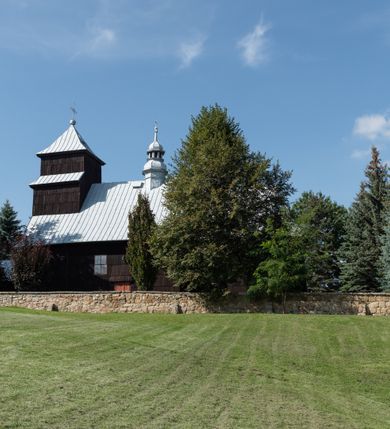 Zdjęcie nr 13: Kościół drewniany o konstrukcji zrębowej, elewacje jednolite, szalowane gontem. Wieża i kruchta zachodnia o konstrukcji słupowo-ramowej, narożne słupy nośne wzmocnione krzyżami św. Andrzeja. Więźba dachowa drewniana, krokwiowa. Budynek na kamiennym podmurowaniu. 
Kościół orientowany, jednonawowy, nawa na rzucie prostokąta zbliżonego do kwadratu, prezbiterium nieco węższe, wydłużone, zakończone trójbocznie. Do północnej ściany prezbiterium przylega zakrystia na planie prostokąta. Przy zachodniej ścianie nawy wieża na planie zbliżonym do prostokąta, o lekko ukośnej ścianie południowej. Od zachodu do wieży przylega kruchta na rzucie prostokąta. 
W przyziemiu wieży babiniec połączony z nawą wtórnym otworem w ścianie. Pomiędzy nawą a prezbiterium otwór tęczowy. Parapet chóru muzycznego w zachodniej części nawy, wsparty na czterech drewnianych kolumnach, z wejściem z nawy po drabiniastych schodach. Ściany i sklepienia pokryte polichromią z iluzjonistyczną architekturą i scenami figuralnymi. Wnętrze nakryte pułapami deskowymi w nawie i prezbiterium oraz stropem belkowym w babińcu. Otwory drzwiowe o prostokątnym wykroju zamknięte drzwiami obitymi deskami w kruchcie zachodniej, w ścianie południowej nawy oraz z prezbiterium do zakrystii. Okna w formie stojącego prostokąta. Posadzka kamienna, z płyt marmurowych. 
Elewacja frontowa jednoosiowa. Na osi wejście do kruchty zachodniej. Korpus wieży podzielony poziomo daszkami okapowymi, na froncie okno. Elewacje boczne jednolite. Korpus nawowy przepruty oknami po dwa na ścianach północnej i południowej, prezbiterium z oknem na ścianie południowej oraz dwoma okienkami na ścianach zamknięcia. Na elewacji wschodniej zawieszony krucyfiks. 
Kościół nakryty dachami dwuspadowymi, o pokryciu blaszanym, wyższym nad nawą, niższym nad prezbiterium. W połowie długości dachu, nad nawą, wbudowana wieżyczka na sygnaturkę, na ośmiobocznym, obitym blachą trzonie, z latarnią zwieńczoną niewielkim hełmem. Wieża nakryta czterospadowym daszkiem namiotowym, zwieńczona kulistą puszką i krzyżem. Kruchta nakryta osobnym daszkiem dwuspadowym, półszczytowym, zakrystia niższym dachem pulpitowym.
