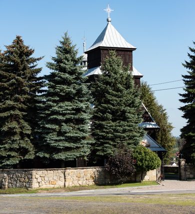 Zdjęcie nr 57: Kościół drewniany o konstrukcji zrębowej, elewacje jednolite, szalowane gontem. Wieża i kruchta zachodnia o konstrukcji słupowo-ramowej, narożne słupy nośne wzmocnione krzyżami św. Andrzeja. Więźba dachowa drewniana, krokwiowa. Budynek na kamiennym podmurowaniu. 
Kościół orientowany, jednonawowy, nawa na rzucie prostokąta zbliżonego do kwadratu, prezbiterium nieco węższe, wydłużone, zakończone trójbocznie. Do północnej ściany prezbiterium przylega zakrystia na planie prostokąta. Przy zachodniej ścianie nawy wieża na planie zbliżonym do prostokąta, o lekko ukośnej ścianie południowej. Od zachodu do wieży przylega kruchta na rzucie prostokąta. 
W przyziemiu wieży babiniec połączony z nawą wtórnym otworem w ścianie. Pomiędzy nawą a prezbiterium otwór tęczowy. Parapet chóru muzycznego w zachodniej części nawy, wsparty na czterech drewnianych kolumnach, z wejściem z nawy po drabiniastych schodach. Ściany i sklepienia pokryte polichromią z iluzjonistyczną architekturą i scenami figuralnymi. Wnętrze nakryte pułapami deskowymi w nawie i prezbiterium oraz stropem belkowym w babińcu. Otwory drzwiowe o prostokątnym wykroju zamknięte drzwiami obitymi deskami w kruchcie zachodniej, w ścianie południowej nawy oraz z prezbiterium do zakrystii. Okna w formie stojącego prostokąta. Posadzka kamienna, z płyt marmurowych. 
Elewacja frontowa jednoosiowa. Na osi wejście do kruchty zachodniej. Korpus wieży podzielony poziomo daszkami okapowymi, na froncie okno. Elewacje boczne jednolite. Korpus nawowy przepruty oknami po dwa na ścianach północnej i południowej, prezbiterium z oknem na ścianie południowej oraz dwoma okienkami na ścianach zamknięcia. Na elewacji wschodniej zawieszony krucyfiks. 
Kościół nakryty dachami dwuspadowymi, o pokryciu blaszanym, wyższym nad nawą, niższym nad prezbiterium. W połowie długości dachu, nad nawą, wbudowana wieżyczka na sygnaturkę, na ośmiobocznym, obitym blachą trzonie, z latarnią zwieńczoną niewielkim hełmem. Wieża nakryta czterospadowym daszkiem namiotowym, zwieńczona kulistą puszką i krzyżem. Kruchta nakryta osobnym daszkiem dwuspadowym, półszczytowym, zakrystia niższym dachem pulpitowym.
