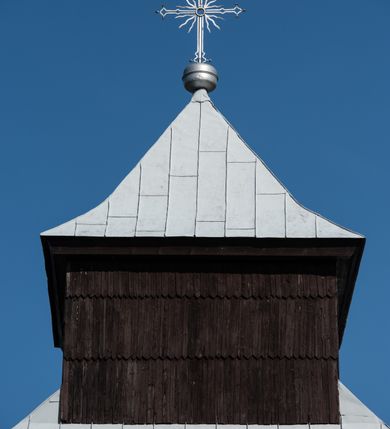 Zdjęcie nr 26: Kościół drewniany o konstrukcji zrębowej, elewacje jednolite, szalowane gontem. Wieża i kruchta zachodnia o konstrukcji słupowo-ramowej, narożne słupy nośne wzmocnione krzyżami św. Andrzeja. Więźba dachowa drewniana, krokwiowa. Budynek na kamiennym podmurowaniu. 
Kościół orientowany, jednonawowy, nawa na rzucie prostokąta zbliżonego do kwadratu, prezbiterium nieco węższe, wydłużone, zakończone trójbocznie. Do północnej ściany prezbiterium przylega zakrystia na planie prostokąta. Przy zachodniej ścianie nawy wieża na planie zbliżonym do prostokąta, o lekko ukośnej ścianie południowej. Od zachodu do wieży przylega kruchta na rzucie prostokąta. 
W przyziemiu wieży babiniec połączony z nawą wtórnym otworem w ścianie. Pomiędzy nawą a prezbiterium otwór tęczowy. Parapet chóru muzycznego w zachodniej części nawy, wsparty na czterech drewnianych kolumnach, z wejściem z nawy po drabiniastych schodach. Ściany i sklepienia pokryte polichromią z iluzjonistyczną architekturą i scenami figuralnymi. Wnętrze nakryte pułapami deskowymi w nawie i prezbiterium oraz stropem belkowym w babińcu. Otwory drzwiowe o prostokątnym wykroju zamknięte drzwiami obitymi deskami w kruchcie zachodniej, w ścianie południowej nawy oraz z prezbiterium do zakrystii. Okna w formie stojącego prostokąta. Posadzka kamienna, z płyt marmurowych. 
Elewacja frontowa jednoosiowa. Na osi wejście do kruchty zachodniej. Korpus wieży podzielony poziomo daszkami okapowymi, na froncie okno. Elewacje boczne jednolite. Korpus nawowy przepruty oknami po dwa na ścianach północnej i południowej, prezbiterium z oknem na ścianie południowej oraz dwoma okienkami na ścianach zamknięcia. Na elewacji wschodniej zawieszony krucyfiks. 
Kościół nakryty dachami dwuspadowymi, o pokryciu blaszanym, wyższym nad nawą, niższym nad prezbiterium. W połowie długości dachu, nad nawą, wbudowana wieżyczka na sygnaturkę, na ośmiobocznym, obitym blachą trzonie, z latarnią zwieńczoną niewielkim hełmem. Wieża nakryta czterospadowym daszkiem namiotowym, zwieńczona kulistą puszką i krzyżem. Kruchta nakryta osobnym daszkiem dwuspadowym, półszczytowym, zakrystia niższym dachem pulpitowym.
