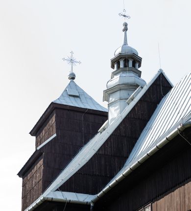 Zdjęcie nr 18: Kościół drewniany o konstrukcji zrębowej, elewacje jednolite, szalowane gontem. Wieża i kruchta zachodnia o konstrukcji słupowo-ramowej, narożne słupy nośne wzmocnione krzyżami św. Andrzeja. Więźba dachowa drewniana, krokwiowa. Budynek na kamiennym podmurowaniu. 
Kościół orientowany, jednonawowy, nawa na rzucie prostokąta zbliżonego do kwadratu, prezbiterium nieco węższe, wydłużone, zakończone trójbocznie. Do północnej ściany prezbiterium przylega zakrystia na planie prostokąta. Przy zachodniej ścianie nawy wieża na planie zbliżonym do prostokąta, o lekko ukośnej ścianie południowej. Od zachodu do wieży przylega kruchta na rzucie prostokąta. 
W przyziemiu wieży babiniec połączony z nawą wtórnym otworem w ścianie. Pomiędzy nawą a prezbiterium otwór tęczowy. Parapet chóru muzycznego w zachodniej części nawy, wsparty na czterech drewnianych kolumnach, z wejściem z nawy po drabiniastych schodach. Ściany i sklepienia pokryte polichromią z iluzjonistyczną architekturą i scenami figuralnymi. Wnętrze nakryte pułapami deskowymi w nawie i prezbiterium oraz stropem belkowym w babińcu. Otwory drzwiowe o prostokątnym wykroju zamknięte drzwiami obitymi deskami w kruchcie zachodniej, w ścianie południowej nawy oraz z prezbiterium do zakrystii. Okna w formie stojącego prostokąta. Posadzka kamienna, z płyt marmurowych. 
Elewacja frontowa jednoosiowa. Na osi wejście do kruchty zachodniej. Korpus wieży podzielony poziomo daszkami okapowymi, na froncie okno. Elewacje boczne jednolite. Korpus nawowy przepruty oknami po dwa na ścianach północnej i południowej, prezbiterium z oknem na ścianie południowej oraz dwoma okienkami na ścianach zamknięcia. Na elewacji wschodniej zawieszony krucyfiks. 
Kościół nakryty dachami dwuspadowymi, o pokryciu blaszanym, wyższym nad nawą, niższym nad prezbiterium. W połowie długości dachu, nad nawą, wbudowana wieżyczka na sygnaturkę, na ośmiobocznym, obitym blachą trzonie, z latarnią zwieńczoną niewielkim hełmem. Wieża nakryta czterospadowym daszkiem namiotowym, zwieńczona kulistą puszką i krzyżem. Kruchta nakryta osobnym daszkiem dwuspadowym, półszczytowym, zakrystia niższym dachem pulpitowym.
