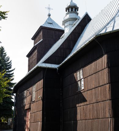 Zdjęcie nr 12: Kościół drewniany o konstrukcji zrębowej, elewacje jednolite, szalowane gontem. Wieża i kruchta zachodnia o konstrukcji słupowo-ramowej, narożne słupy nośne wzmocnione krzyżami św. Andrzeja. Więźba dachowa drewniana, krokwiowa. Budynek na kamiennym podmurowaniu. 
Kościół orientowany, jednonawowy, nawa na rzucie prostokąta zbliżonego do kwadratu, prezbiterium nieco węższe, wydłużone, zakończone trójbocznie. Do północnej ściany prezbiterium przylega zakrystia na planie prostokąta. Przy zachodniej ścianie nawy wieża na planie zbliżonym do prostokąta, o lekko ukośnej ścianie południowej. Od zachodu do wieży przylega kruchta na rzucie prostokąta. 
W przyziemiu wieży babiniec połączony z nawą wtórnym otworem w ścianie. Pomiędzy nawą a prezbiterium otwór tęczowy. Parapet chóru muzycznego w zachodniej części nawy, wsparty na czterech drewnianych kolumnach, z wejściem z nawy po drabiniastych schodach. Ściany i sklepienia pokryte polichromią z iluzjonistyczną architekturą i scenami figuralnymi. Wnętrze nakryte pułapami deskowymi w nawie i prezbiterium oraz stropem belkowym w babińcu. Otwory drzwiowe o prostokątnym wykroju zamknięte drzwiami obitymi deskami w kruchcie zachodniej, w ścianie południowej nawy oraz z prezbiterium do zakrystii. Okna w formie stojącego prostokąta. Posadzka kamienna, z płyt marmurowych. 
Elewacja frontowa jednoosiowa. Na osi wejście do kruchty zachodniej. Korpus wieży podzielony poziomo daszkami okapowymi, na froncie okno. Elewacje boczne jednolite. Korpus nawowy przepruty oknami po dwa na ścianach północnej i południowej, prezbiterium z oknem na ścianie południowej oraz dwoma okienkami na ścianach zamknięcia. Na elewacji wschodniej zawieszony krucyfiks. 
Kościół nakryty dachami dwuspadowymi, o pokryciu blaszanym, wyższym nad nawą, niższym nad prezbiterium. W połowie długości dachu, nad nawą, wbudowana wieżyczka na sygnaturkę, na ośmiobocznym, obitym blachą trzonie, z latarnią zwieńczoną niewielkim hełmem. Wieża nakryta czterospadowym daszkiem namiotowym, zwieńczona kulistą puszką i krzyżem. Kruchta nakryta osobnym daszkiem dwuspadowym, półszczytowym, zakrystia niższym dachem pulpitowym.

