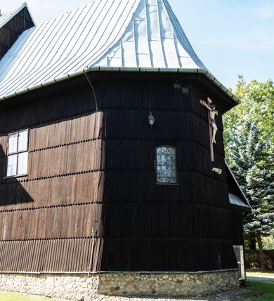 Zdjęcie nr 21: Kościół drewniany o konstrukcji zrębowej, elewacje jednolite, szalowane gontem. Wieża i kruchta zachodnia o konstrukcji słupowo-ramowej, narożne słupy nośne wzmocnione krzyżami św. Andrzeja. Więźba dachowa drewniana, krokwiowa. Budynek na kamiennym podmurowaniu. 
Kościół orientowany, jednonawowy, nawa na rzucie prostokąta zbliżonego do kwadratu, prezbiterium nieco węższe, wydłużone, zakończone trójbocznie. Do północnej ściany prezbiterium przylega zakrystia na planie prostokąta. Przy zachodniej ścianie nawy wieża na planie zbliżonym do prostokąta, o lekko ukośnej ścianie południowej. Od zachodu do wieży przylega kruchta na rzucie prostokąta. 
W przyziemiu wieży babiniec połączony z nawą wtórnym otworem w ścianie. Pomiędzy nawą a prezbiterium otwór tęczowy. Parapet chóru muzycznego w zachodniej części nawy, wsparty na czterech drewnianych kolumnach, z wejściem z nawy po drabiniastych schodach. Ściany i sklepienia pokryte polichromią z iluzjonistyczną architekturą i scenami figuralnymi. Wnętrze nakryte pułapami deskowymi w nawie i prezbiterium oraz stropem belkowym w babińcu. Otwory drzwiowe o prostokątnym wykroju zamknięte drzwiami obitymi deskami w kruchcie zachodniej, w ścianie południowej nawy oraz z prezbiterium do zakrystii. Okna w formie stojącego prostokąta. Posadzka kamienna, z płyt marmurowych. 
Elewacja frontowa jednoosiowa. Na osi wejście do kruchty zachodniej. Korpus wieży podzielony poziomo daszkami okapowymi, na froncie okno. Elewacje boczne jednolite. Korpus nawowy przepruty oknami po dwa na ścianach północnej i południowej, prezbiterium z oknem na ścianie południowej oraz dwoma okienkami na ścianach zamknięcia. Na elewacji wschodniej zawieszony krucyfiks. 
Kościół nakryty dachami dwuspadowymi, o pokryciu blaszanym, wyższym nad nawą, niższym nad prezbiterium. W połowie długości dachu, nad nawą, wbudowana wieżyczka na sygnaturkę, na ośmiobocznym, obitym blachą trzonie, z latarnią zwieńczoną niewielkim hełmem. Wieża nakryta czterospadowym daszkiem namiotowym, zwieńczona kulistą puszką i krzyżem. Kruchta nakryta osobnym daszkiem dwuspadowym, półszczytowym, zakrystia niższym dachem pulpitowym.
