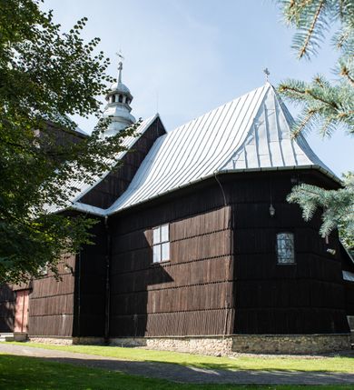 Zdjęcie nr 10: Kościół drewniany o konstrukcji zrębowej, elewacje jednolite, szalowane gontem. Wieża i kruchta zachodnia o konstrukcji słupowo-ramowej, narożne słupy nośne wzmocnione krzyżami św. Andrzeja. Więźba dachowa drewniana, krokwiowa. Budynek na kamiennym podmurowaniu. 
Kościół orientowany, jednonawowy, nawa na rzucie prostokąta zbliżonego do kwadratu, prezbiterium nieco węższe, wydłużone, zakończone trójbocznie. Do północnej ściany prezbiterium przylega zakrystia na planie prostokąta. Przy zachodniej ścianie nawy wieża na planie zbliżonym do prostokąta, o lekko ukośnej ścianie południowej. Od zachodu do wieży przylega kruchta na rzucie prostokąta. 
W przyziemiu wieży babiniec połączony z nawą wtórnym otworem w ścianie. Pomiędzy nawą a prezbiterium otwór tęczowy. Parapet chóru muzycznego w zachodniej części nawy, wsparty na czterech drewnianych kolumnach, z wejściem z nawy po drabiniastych schodach. Ściany i sklepienia pokryte polichromią z iluzjonistyczną architekturą i scenami figuralnymi. Wnętrze nakryte pułapami deskowymi w nawie i prezbiterium oraz stropem belkowym w babińcu. Otwory drzwiowe o prostokątnym wykroju zamknięte drzwiami obitymi deskami w kruchcie zachodniej, w ścianie południowej nawy oraz z prezbiterium do zakrystii. Okna w formie stojącego prostokąta. Posadzka kamienna, z płyt marmurowych. 
Elewacja frontowa jednoosiowa. Na osi wejście do kruchty zachodniej. Korpus wieży podzielony poziomo daszkami okapowymi, na froncie okno. Elewacje boczne jednolite. Korpus nawowy przepruty oknami po dwa na ścianach północnej i południowej, prezbiterium z oknem na ścianie południowej oraz dwoma okienkami na ścianach zamknięcia. Na elewacji wschodniej zawieszony krucyfiks. 
Kościół nakryty dachami dwuspadowymi, o pokryciu blaszanym, wyższym nad nawą, niższym nad prezbiterium. W połowie długości dachu, nad nawą, wbudowana wieżyczka na sygnaturkę, na ośmiobocznym, obitym blachą trzonie, z latarnią zwieńczoną niewielkim hełmem. Wieża nakryta czterospadowym daszkiem namiotowym, zwieńczona kulistą puszką i krzyżem. Kruchta nakryta osobnym daszkiem dwuspadowym, półszczytowym, zakrystia niższym dachem pulpitowym.
