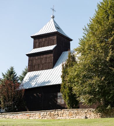 Zdjęcie nr 9: Kościół drewniany o konstrukcji zrębowej, elewacje jednolite, szalowane gontem. Wieża i kruchta zachodnia o konstrukcji słupowo-ramowej, narożne słupy nośne wzmocnione krzyżami św. Andrzeja. Więźba dachowa drewniana, krokwiowa. Budynek na kamiennym podmurowaniu. 
Kościół orientowany, jednonawowy, nawa na rzucie prostokąta zbliżonego do kwadratu, prezbiterium nieco węższe, wydłużone, zakończone trójbocznie. Do północnej ściany prezbiterium przylega zakrystia na planie prostokąta. Przy zachodniej ścianie nawy wieża na planie zbliżonym do prostokąta, o lekko ukośnej ścianie południowej. Od zachodu do wieży przylega kruchta na rzucie prostokąta. 
W przyziemiu wieży babiniec połączony z nawą wtórnym otworem w ścianie. Pomiędzy nawą a prezbiterium otwór tęczowy. Parapet chóru muzycznego w zachodniej części nawy, wsparty na czterech drewnianych kolumnach, z wejściem z nawy po drabiniastych schodach. Ściany i sklepienia pokryte polichromią z iluzjonistyczną architekturą i scenami figuralnymi. Wnętrze nakryte pułapami deskowymi w nawie i prezbiterium oraz stropem belkowym w babińcu. Otwory drzwiowe o prostokątnym wykroju zamknięte drzwiami obitymi deskami w kruchcie zachodniej, w ścianie południowej nawy oraz z prezbiterium do zakrystii. Okna w formie stojącego prostokąta. Posadzka kamienna, z płyt marmurowych. 
Elewacja frontowa jednoosiowa. Na osi wejście do kruchty zachodniej. Korpus wieży podzielony poziomo daszkami okapowymi, na froncie okno. Elewacje boczne jednolite. Korpus nawowy przepruty oknami po dwa na ścianach północnej i południowej, prezbiterium z oknem na ścianie południowej oraz dwoma okienkami na ścianach zamknięcia. Na elewacji wschodniej zawieszony krucyfiks. 
Kościół nakryty dachami dwuspadowymi, o pokryciu blaszanym, wyższym nad nawą, niższym nad prezbiterium. W połowie długości dachu, nad nawą, wbudowana wieżyczka na sygnaturkę, na ośmiobocznym, obitym blachą trzonie, z latarnią zwieńczoną niewielkim hełmem. Wieża nakryta czterospadowym daszkiem namiotowym, zwieńczona kulistą puszką i krzyżem. Kruchta nakryta osobnym daszkiem dwuspadowym, półszczytowym, zakrystia niższym dachem pulpitowym.
