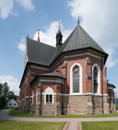 Zdjęcie nr 12: Kościół orientowany, składający się trójnawowej, czteroprzęsłowej pseudohali z transeptem oraz z jednoprzęsłowym, zamkniętym trójbocznie prezbiterium, przy którym od północy usytuowana jest zakrystia, a od południa skarbiec, zamknięte dwubocznie. Od fasady, na przedłużeniu nawy, usytuowana jest czteroboczna wieża, a przy niej ośmioboczne wieżyczki schodowe. Kościół ustawiony jest na wysokim, kamiennym cokole. Wieża trójkondygnacyjna: w dolnej kondygnacji ostrołukowy portal w obramieniu z kolumienkami i wimpergą, nad nim rozeta; w drugiej, ostrołukowe okno z maswerkiem; w trzeciej tryforium. Ściany wieży są zwieńczone szczytami, a wieżyczki schodowe ostrosłupowymi ceglanymi hełmami. Elewacje opięte są przyporami, zwieńczone gzymsem. Okna ostrołukowe z maswerkami, w tynkowanych na biało obramieniach. Dachy dwuspadowe, nad zakrystią i skarbcem pulpitowe, hełm wieży ostrosłupowy; pokrycie blachą. Empora organowa znajduje się w zachodnim przęśle nawy. Sklepienia krzyżowo-żebrowe, przy prezbiterium – gwiaździste. Nawy oddzielone kolumnami o kapitelach pączkowych; na ścianach naw bocznych pilastry. Chór muzyczny na kolumnach z kapitelami kostkowymi. Okna prostokątne zakończone ostrołukowo, w prezbiterium: jednodzielne, usytuowane w trzech ścianach zamknięcia chóru, z witrażami; w korpusie nawowym: trój- i dwudzielne, w pierwszych (wschodnich) trzech przęsłach z witrażami. Żebra sklepienne podkreślone polichromią. Portal główny zdobi tondo z płaskorzeźbą Najświętszego Serca Pana Jezusa.