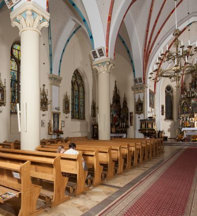 Zdjęcie nr 20: Kościół orientowany, składający się trójnawowej, czteroprzęsłowej pseudohali z transeptem oraz z jednoprzęsłowym, zamkniętym trójbocznie prezbiterium, przy którym od północy usytuowana jest zakrystia, a od południa skarbiec, zamknięte dwubocznie. Od fasady, na przedłużeniu nawy, usytuowana jest czteroboczna wieża, a przy niej ośmioboczne wieżyczki schodowe. Kościół ustawiony jest na wysokim, kamiennym cokole. Wieża trójkondygnacyjna: w dolnej kondygnacji ostrołukowy portal w obramieniu z kolumienkami i wimpergą, nad nim rozeta; w drugiej, ostrołukowe okno z maswerkiem; w trzeciej tryforium. Ściany wieży są zwieńczone szczytami, a wieżyczki schodowe ostrosłupowymi ceglanymi hełmami. Elewacje opięte są przyporami, zwieńczone gzymsem. Okna ostrołukowe z maswerkami, w tynkowanych na biało obramieniach. Dachy dwuspadowe, nad zakrystią i skarbcem pulpitowe, hełm wieży ostrosłupowy; pokrycie blachą. Empora organowa znajduje się w zachodnim przęśle nawy. Sklepienia krzyżowo-żebrowe, przy prezbiterium – gwiaździste. Nawy oddzielone kolumnami o kapitelach pączkowych; na ścianach naw bocznych pilastry. Chór muzyczny na kolumnach z kapitelami kostkowymi. Okna prostokątne zakończone ostrołukowo, w prezbiterium: jednodzielne, usytuowane w trzech ścianach zamknięcia chóru, z witrażami; w korpusie nawowym: trój- i dwudzielne, w pierwszych (wschodnich) trzech przęsłach z witrażami. Żebra sklepienne podkreślone polichromią. Portal główny zdobi tondo z płaskorzeźbą Najświętszego Serca Pana Jezusa.