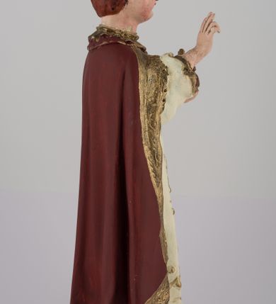 Zdjęcie nr 4: Rzeźba pełnoplastyczna, przedstawiająca stojące na profilowanej podstawie Dzieciątko Jezus. Wzrok skierowany przed siebie, nos mały, prosty, usta pełne, kości policzkowe wydatne. Włosy brązowe, na głowie bordowa, zamknięta korona ze złotymi elementami. Prawa ręka wyciągnięta w geście błogosławieństwa, w lewej królewskie jabłko. Tunika biała z długimi rękawami, zdobiona monogramem IHS z promieniami na piersi, wicią kwiatową oraz złotą lamówką. Płaszcz bordowy ze złotym wykończeniem spięty pod szyją. Szaty płasko fałdowane. Polichromia w partiach ciała naturalistyczna.