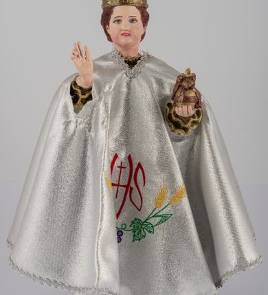 Zdjęcie nr 6: Rzeźba pełnoplastyczna, przedstawiająca stojące na profilowanej podstawie Dzieciątko Jezus. Wzrok skierowany przed siebie, nos mały, prosty, usta pełne, kości policzkowe wydatne. Włosy brązowe, na głowie bordowa, zamknięta korona ze złotymi elementami. Prawa ręka wyciągnięta w geście błogosławieństwa, w lewej królewskie jabłko. Tunika biała z długimi rękawami, zdobiona monogramem IHS z promieniami na piersi, wicią kwiatową oraz złotą lamówką. Płaszcz bordowy ze złotym wykończeniem spięty pod szyją. Szaty płasko fałdowane. Polichromia w partiach ciała naturalistyczna.