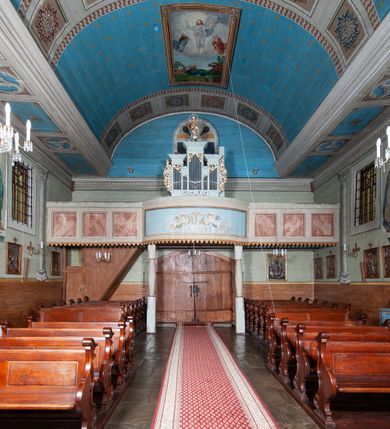 Zdjęcie nr 58: Kościół orientowany, drewniany, na podmurowaniu, o konstrukcji zrębowej, z wieżą o konstrukcji słupowo-ramowej. Składa się z prostokątnej nawy, do której od wschodu przylega węższe prezbiterium zamknięte trójbocznie. Do niego od północy dobudowano prostokątną zakrystię. Do nawy od zachodu przylega wieża na rzucie kwadratu, o ścianach pochyłych, rozdzielona na kondygnacje daszkiem; zwieńczona nadwieszoną izbicą szalowaną pionowymi deskami wyciętymi dołem w ozdobną koronkę; w ścianach izbicy po dwa małe okienka. 
Kościół jednonawowy, z węższym prezbiterium oddzielonym ścianą tęczową. Otwór tęczowy podwójny, górny mniejszy, w strefie sklepień, dolny większy, wycięty w zrębie. Na podniebiu dolnego łuku napis „TEN KOŚCIÓŁ ZAŁOŻONY RP 1789 BENEDYKOWANY RP 1792 MALOWANY RP 1930”. Ściany gładkie, pokryte dekoracją malarską imitującą detale architektoniczne: kolumny, belkowanie, obramienia okien, plafony wypełnione rzeźbiarską dekoracją; między nimi postacie świętych. W nawie od zachodu chór muzyczny wsparty na dwóch, profilowanych słupach, z parapetem wybrzuszonym pośrodku. Nawa i prezbiterium nakryte pozornym sklepieniem kolebkowym z płaskimi odcinkami stropowymi po bokach. 
W nawie głównej cztery okna, w prezbiterium dwa, wszystkie w kształcie stojącego prostokąta; w dolnej kondygnacji wieży dwa okna w kształcie leżącego prostokąta. Wejście główne od zachodu, kolejne od południa, oba portale zamknięte od góry łukiem „w ośli grzbiet”; portal z prezbiterium do zakrystii.  
Kościół obiegają soboty, czyli rodzaj podcieni, zamkniętych wokół wieży, otwartych na pozostałej długości; z kruchtami od zachodu i od południa; cztery kwadratowe okienka w sobotach od zachodu. 
Ściany na zewnątrz kościoła pobite deskami. Nad nawą główną dach dwuspadowy, nad prezbiterium wielopołaciowy, przedłużony od północy na zakrystię. Na dachu nawy zwężająca się ku górze wieżyczka na sygnaturkę, która przechodzi w latarnię o cebulastym zakończeniu. Wieżę zachodnią wieńczy hełm złożony z niskiego dachu namiotowego i nasadzonej na niego bani z kulą i krzyżem. Soboty nakryto dachem pulpitowym, wygiętym przy ścianie wschodniej zakrystii łukowo ku górze po to, aby lepiej ją doświetlić. Dachy kryte gontami, hełmy wież blachą. 
