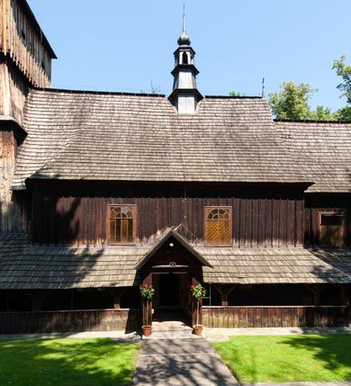 Zdjęcie nr 5: Kościół orientowany, drewniany, na podmurowaniu, o konstrukcji zrębowej, z wieżą o konstrukcji słupowo-ramowej. Składa się z prostokątnej nawy, do której od wschodu przylega węższe prezbiterium zamknięte trójbocznie. Do niego od północy dobudowano prostokątną zakrystię. Do nawy od zachodu przylega wieża na rzucie kwadratu, o ścianach pochyłych, rozdzielona na kondygnacje daszkiem; zwieńczona nadwieszoną izbicą szalowaną pionowymi deskami wyciętymi dołem w ozdobną koronkę; w ścianach izbicy po dwa małe okienka. 
Kościół jednonawowy, z węższym prezbiterium oddzielonym ścianą tęczową. Otwór tęczowy podwójny, górny mniejszy, w strefie sklepień, dolny większy, wycięty w zrębie. Na podniebiu dolnego łuku napis „TEN KOŚCIÓŁ ZAŁOŻONY RP 1789 BENEDYKOWANY RP 1792 MALOWANY RP 1930”. Ściany gładkie, pokryte dekoracją malarską imitującą detale architektoniczne: kolumny, belkowanie, obramienia okien, plafony wypełnione rzeźbiarską dekoracją; między nimi postacie świętych. W nawie od zachodu chór muzyczny wsparty na dwóch, profilowanych słupach, z parapetem wybrzuszonym pośrodku. Nawa i prezbiterium nakryte pozornym sklepieniem kolebkowym z płaskimi odcinkami stropowymi po bokach. 
W nawie głównej cztery okna, w prezbiterium dwa, wszystkie w kształcie stojącego prostokąta; w dolnej kondygnacji wieży dwa okna w kształcie leżącego prostokąta. Wejście główne od zachodu, kolejne od południa, oba portale zamknięte od góry łukiem „w ośli grzbiet”; portal z prezbiterium do zakrystii.  
Kościół obiegają soboty, czyli rodzaj podcieni, zamkniętych wokół wieży, otwartych na pozostałej długości; z kruchtami od zachodu i od południa; cztery kwadratowe okienka w sobotach od zachodu. 
Ściany na zewnątrz kościoła pobite deskami. Nad nawą główną dach dwuspadowy, nad prezbiterium wielopołaciowy, przedłużony od północy na zakrystię. Na dachu nawy zwężająca się ku górze wieżyczka na sygnaturkę, która przechodzi w latarnię o cebulastym zakończeniu. Wieżę zachodnią wieńczy hełm złożony z niskiego dachu namiotowego i nasadzonej na niego bani z kulą i krzyżem. Soboty nakryto dachem pulpitowym, wygiętym przy ścianie wschodniej zakrystii łukowo ku górze po to, aby lepiej ją doświetlić. Dachy kryte gontami, hełmy wież blachą. 
