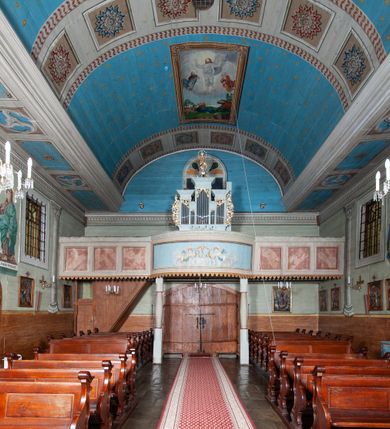 Zdjęcie nr 56: Kościół orientowany, drewniany, na podmurowaniu, o konstrukcji zrębowej, z wieżą o konstrukcji słupowo-ramowej. Składa się z prostokątnej nawy, do której od wschodu przylega węższe prezbiterium zamknięte trójbocznie. Do niego od północy dobudowano prostokątną zakrystię. Do nawy od zachodu przylega wieża na rzucie kwadratu, o ścianach pochyłych, rozdzielona na kondygnacje daszkiem; zwieńczona nadwieszoną izbicą szalowaną pionowymi deskami wyciętymi dołem w ozdobną koronkę; w ścianach izbicy po dwa małe okienka. 
Kościół jednonawowy, z węższym prezbiterium oddzielonym ścianą tęczową. Otwór tęczowy podwójny, górny mniejszy, w strefie sklepień, dolny większy, wycięty w zrębie. Na podniebiu dolnego łuku napis „TEN KOŚCIÓŁ ZAŁOŻONY RP 1789 BENEDYKOWANY RP 1792 MALOWANY RP 1930”. Ściany gładkie, pokryte dekoracją malarską imitującą detale architektoniczne: kolumny, belkowanie, obramienia okien, plafony wypełnione rzeźbiarską dekoracją; między nimi postacie świętych. W nawie od zachodu chór muzyczny wsparty na dwóch, profilowanych słupach, z parapetem wybrzuszonym pośrodku. Nawa i prezbiterium nakryte pozornym sklepieniem kolebkowym z płaskimi odcinkami stropowymi po bokach. 
W nawie głównej cztery okna, w prezbiterium dwa, wszystkie w kształcie stojącego prostokąta; w dolnej kondygnacji wieży dwa okna w kształcie leżącego prostokąta. Wejście główne od zachodu, kolejne od południa, oba portale zamknięte od góry łukiem „w ośli grzbiet”; portal z prezbiterium do zakrystii.  
Kościół obiegają soboty, czyli rodzaj podcieni, zamkniętych wokół wieży, otwartych na pozostałej długości; z kruchtami od zachodu i od południa; cztery kwadratowe okienka w sobotach od zachodu. 
Ściany na zewnątrz kościoła pobite deskami. Nad nawą główną dach dwuspadowy, nad prezbiterium wielopołaciowy, przedłużony od północy na zakrystię. Na dachu nawy zwężająca się ku górze wieżyczka na sygnaturkę, która przechodzi w latarnię o cebulastym zakończeniu. Wieżę zachodnią wieńczy hełm złożony z niskiego dachu namiotowego i nasadzonej na niego bani z kulą i krzyżem. Soboty nakryto dachem pulpitowym, wygiętym przy ścianie wschodniej zakrystii łukowo ku górze po to, aby lepiej ją doświetlić. Dachy kryte gontami, hełmy wież blachą. 
