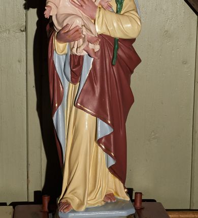 Zdjęcie nr 1: Rzeźba pełna umieszczona na profilowanym cokole umocowanym do prostopadłościennej podstawy z otworami na drążki do noszenia w procesji. Figura przedstawia stojącego frontalnie św. Józefa z Dzieciątkiem Jezus na prawym ręku. Święty został ujęty w lekkim kontrapoście z prawą nogą ugiętą w kolanie. Głowę ma delikatnie opuszczoną, wzrok skierowany w dół, nos prosty, usta wąskie; ciemny zarost oraz włosy zakrywające uszy. Prawą ręką podtrzymuje siedzące Dzieciątko Jezus, lewą dotyka jego torsu. Święty Józef jest ubrany w bladożółtą suknię, na którą ma narzucony czerwony płaszcz z jasnoniebieskim podbiciem dekorowany przy brzegach wąskim, złotym paskiem. Dzieciątko rozkłada ręce na boki. Ma owalną twarz z szerokim czołem, małymi oczami i ustami oraz wąskim nosem. Jego krótkie, jasne włosy układają się w fale. Jest ubrane w długą, jasną sukienkę, lamowaną pod szyją złotem i dekorowaną wąskim paskami przy krawędziach. Polichromia w partiach ciała naturalistyczna.