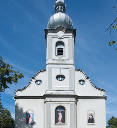 Zdjęcie nr 3: Kościół murowany, jednonawowy, na rzucie prostokąta, z późniejszymi dobudówkami. Prezbiterium usytuowane od północy, jednoprzęsłowe, węższe od korpusu, zamknięte półkolistą absydą. Do prezbiterium dobudowana zakrystia od wschodu oraz kaplica od zachodu poprzedzona niewielką kruchtą. Nawa główna trójprzęsłowa z partią wieżową niewyróżniającą się w bryle. Po bokach przęsła środkowego dostawione dwie kaplice na rzucie kwadratu: od wschodu Matki Boskiej Częstochowskiej, od zachodu św. Maksymiliana Marii Kolbego. Chór muzyczny wsparty na trzech arkadach. W prezbiterium sklepienie żaglaste, a w nawie krzyżowe, pozorne, oddzielone gurtami wychodzącymi z potężnych filarów przyściennych. Okna prostokątne, zamknięte półkoliście znajdują się w nawie, kaplicy przy prezbiterium, w wieży i w ścianach bocznych absydy. Natomiast w ścianach bocznych prezbiterium, na osi absydy i w kaplicach przy nawie okna koliste. Okna w większości wypełnione witrażami ze scenami figuralnymi, w innych ozdobne przeszklenia geometryczne. Fasada trójosiowa, na osi środkowej usytuowana wieża, delikatnie wystająca przed lico fasady, o podziałach ramowych, nakryta baniastym hełmem z dwukondygnacyjną latarnią. Osie boczne zwieńczone spływami wolutowymi. Dachy gontowe.

