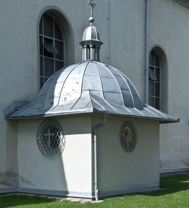 Zdjęcie nr 8: Kościół murowany, jednonawowy, na rzucie prostokąta, z późniejszymi dobudówkami. Prezbiterium usytuowane od północy, jednoprzęsłowe, węższe od korpusu, zamknięte półkolistą absydą. Do prezbiterium dobudowana zakrystia od wschodu oraz kaplica od zachodu poprzedzona niewielką kruchtą. Nawa główna trójprzęsłowa z partią wieżową niewyróżniającą się w bryle. Po bokach przęsła środkowego dostawione dwie kaplice na rzucie kwadratu: od wschodu Matki Boskiej Częstochowskiej, od zachodu św. Maksymiliana Marii Kolbego. Chór muzyczny wsparty na trzech arkadach. W prezbiterium sklepienie żaglaste, a w nawie krzyżowe, pozorne, oddzielone gurtami wychodzącymi z potężnych filarów przyściennych. Okna prostokątne, zamknięte półkoliście znajdują się w nawie, kaplicy przy prezbiterium, w wieży i w ścianach bocznych absydy. Natomiast w ścianach bocznych prezbiterium, na osi absydy i w kaplicach przy nawie okna koliste. Okna w większości wypełnione witrażami ze scenami figuralnymi, w innych ozdobne przeszklenia geometryczne. Fasada trójosiowa, na osi środkowej usytuowana wieża, delikatnie wystająca przed lico fasady, o podziałach ramowych, nakryta baniastym hełmem z dwukondygnacyjną latarnią. Osie boczne zwieńczone spływami wolutowymi. Dachy gontowe.

