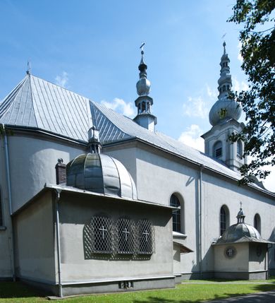 Zdjęcie nr 4: Kościół murowany, jednonawowy, na rzucie prostokąta, z późniejszymi dobudówkami. Prezbiterium usytuowane od północy, jednoprzęsłowe, węższe od korpusu, zamknięte półkolistą absydą. Do prezbiterium dobudowana zakrystia od wschodu oraz kaplica od zachodu poprzedzona niewielką kruchtą. Nawa główna trójprzęsłowa z partią wieżową niewyróżniającą się w bryle. Po bokach przęsła środkowego dostawione dwie kaplice na rzucie kwadratu: od wschodu Matki Boskiej Częstochowskiej, od zachodu św. Maksymiliana Marii Kolbego. Chór muzyczny wsparty na trzech arkadach. W prezbiterium sklepienie żaglaste, a w nawie krzyżowe, pozorne, oddzielone gurtami wychodzącymi z potężnych filarów przyściennych. Okna prostokątne, zamknięte półkoliście znajdują się w nawie, kaplicy przy prezbiterium, w wieży i w ścianach bocznych absydy. Natomiast w ścianach bocznych prezbiterium, na osi absydy i w kaplicach przy nawie okna koliste. Okna w większości wypełnione witrażami ze scenami figuralnymi, w innych ozdobne przeszklenia geometryczne. Fasada trójosiowa, na osi środkowej usytuowana wieża, delikatnie wystająca przed lico fasady, o podziałach ramowych, nakryta baniastym hełmem z dwukondygnacyjną latarnią. Osie boczne zwieńczone spływami wolutowymi. Dachy gontowe.

