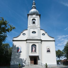 Zdjęcie nr 1: Kościół murowany, jednonawowy, na rzucie prostokąta, z późniejszymi dobudówkami. Prezbiterium usytuowane od północy, jednoprzęsłowe, węższe od korpusu, zamknięte półkolistą absydą. Do prezbiterium dobudowana zakrystia od wschodu oraz kaplica od zachodu poprzedzona niewielką kruchtą. Nawa główna trójprzęsłowa z partią wieżową niewyróżniającą się w bryle. Po bokach przęsła środkowego dostawione dwie kaplice na rzucie kwadratu: od wschodu Matki Boskiej Częstochowskiej, od zachodu św. Maksymiliana Marii Kolbego. Chór muzyczny wsparty na trzech arkadach. W prezbiterium sklepienie żaglaste, a w nawie krzyżowe, pozorne, oddzielone gurtami wychodzącymi z potężnych filarów przyściennych. Okna prostokątne, zamknięte półkoliście znajdują się w nawie, kaplicy przy prezbiterium, w wieży i w ścianach bocznych absydy. Natomiast w ścianach bocznych prezbiterium, na osi absydy i w kaplicach przy nawie okna koliste. Okna w większości wypełnione witrażami ze scenami figuralnymi, w innych ozdobne przeszklenia geometryczne. Fasada trójosiowa, na osi środkowej usytuowana wieża, delikatnie wystająca przed lico fasady, o podziałach ramowych, nakryta baniastym hełmem z dwukondygnacyjną latarnią. Osie boczne zwieńczone spływami wolutowymi. Dachy gontowe.

