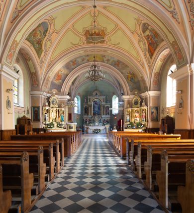 Zdjęcie nr 10: Kościół murowany, jednonawowy, na rzucie prostokąta, z późniejszymi dobudówkami. Prezbiterium usytuowane od północy, jednoprzęsłowe, węższe od korpusu, zamknięte półkolistą absydą. Do prezbiterium dobudowana zakrystia od wschodu oraz kaplica od zachodu poprzedzona niewielką kruchtą. Nawa główna trójprzęsłowa z partią wieżową niewyróżniającą się w bryle. Po bokach przęsła środkowego dostawione dwie kaplice na rzucie kwadratu: od wschodu Matki Boskiej Częstochowskiej, od zachodu św. Maksymiliana Marii Kolbego. Chór muzyczny wsparty na trzech arkadach. W prezbiterium sklepienie żaglaste, a w nawie krzyżowe, pozorne, oddzielone gurtami wychodzącymi z potężnych filarów przyściennych. Okna prostokątne, zamknięte półkoliście znajdują się w nawie, kaplicy przy prezbiterium, w wieży i w ścianach bocznych absydy. Natomiast w ścianach bocznych prezbiterium, na osi absydy i w kaplicach przy nawie okna koliste. Okna w większości wypełnione witrażami ze scenami figuralnymi, w innych ozdobne przeszklenia geometryczne. Fasada trójosiowa, na osi środkowej usytuowana wieża, delikatnie wystająca przed lico fasady, o podziałach ramowych, nakryta baniastym hełmem z dwukondygnacyjną latarnią. Osie boczne zwieńczone spływami wolutowymi. Dachy gontowe.

